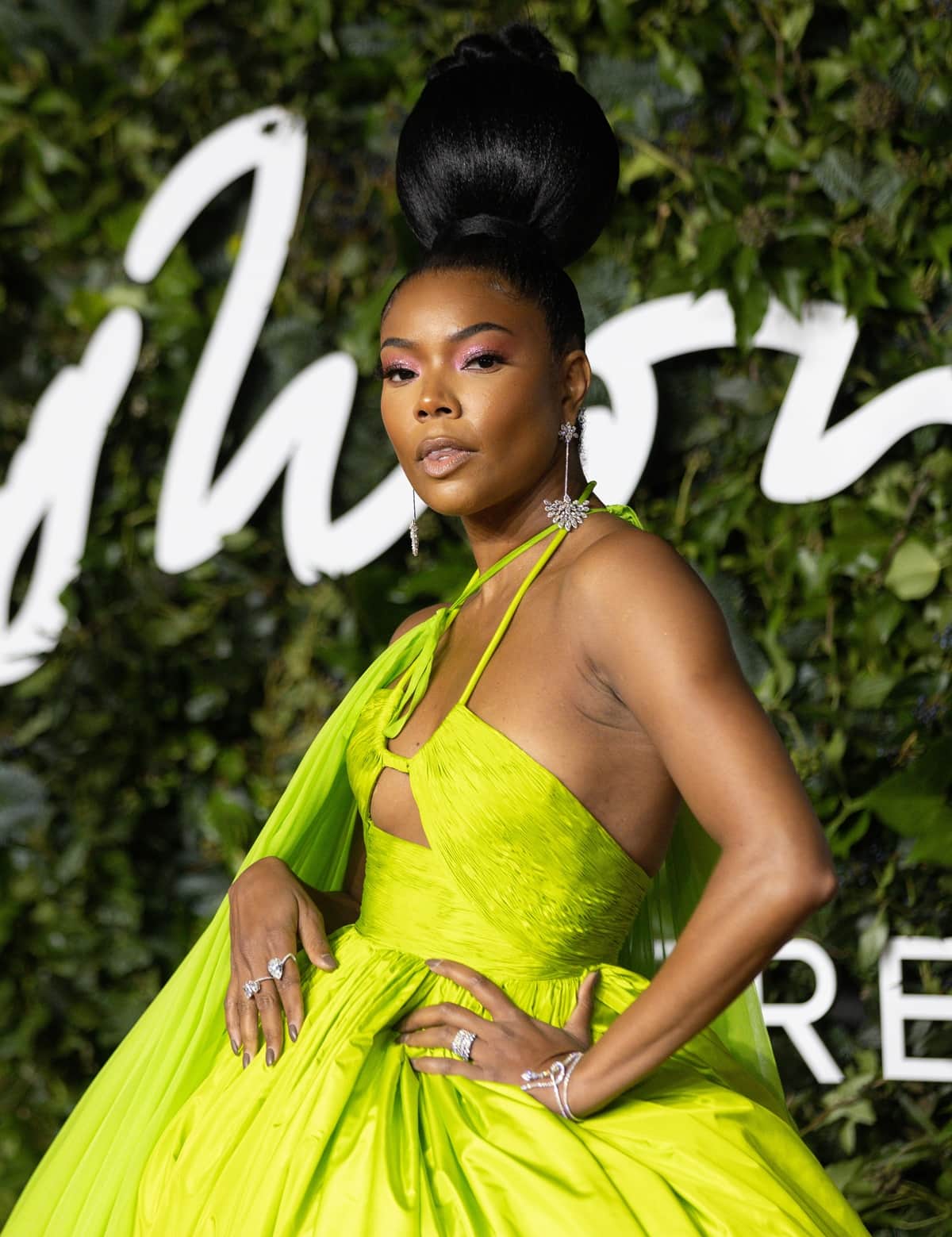 Gabrielle Union elevated her neon Valentino moment with a sculptural, high-set bun and sparkling diamond drop earrings, letting the clean, polished beauty look frame the gown’s dramatic silhouette