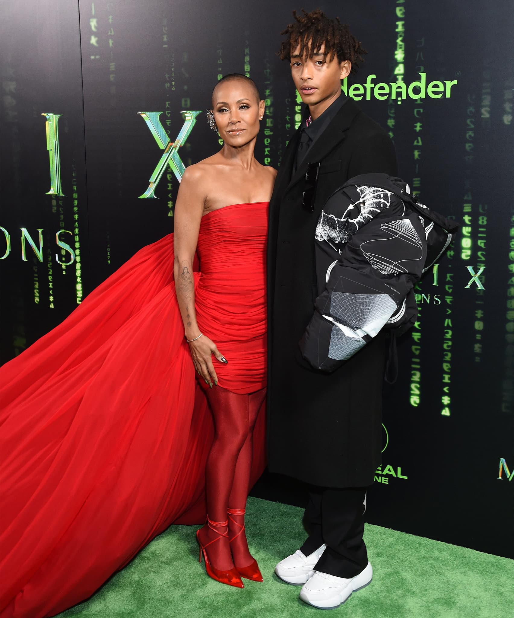 Standing beside Jaden Smith’s relaxed black tailoring and chunky white sneakers, Jada’s sculpted red look—anchored by sleek PVC pumps—delivers a striking study in contrast between precision and ease