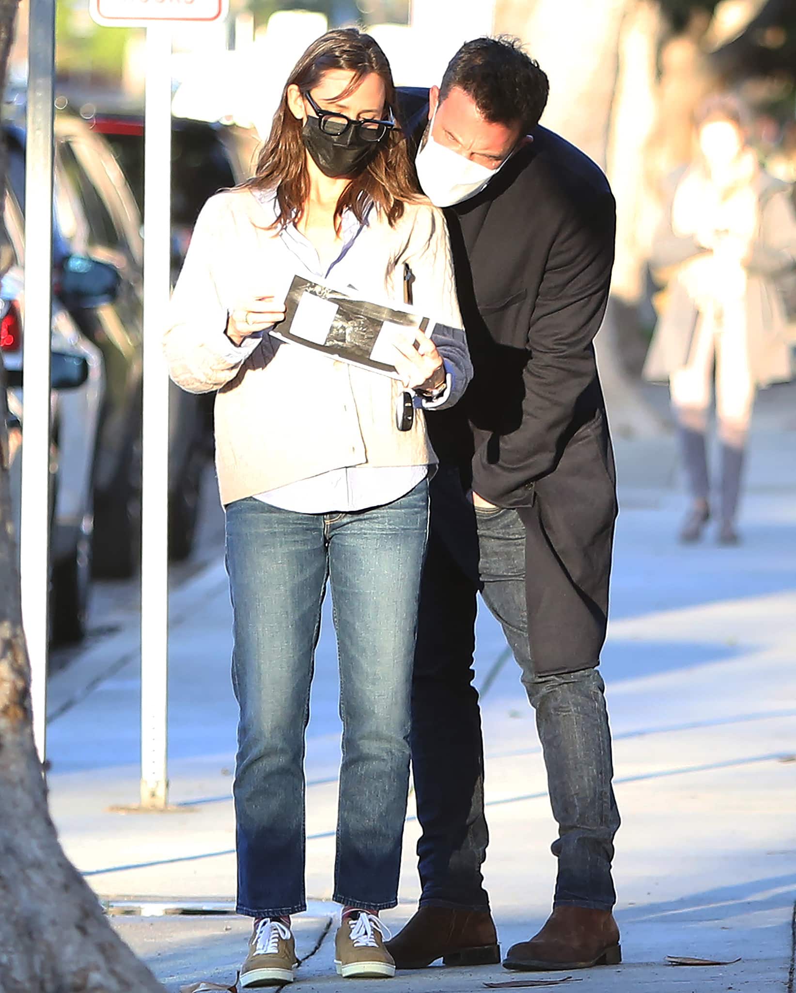 Jennifer Garner paired cropped blue jeans with Chanel suede calfskin sneakers, a cream cable-knit cardigan, and Jacques Marie Mage “Jax” eyeglasses, while Ben Affleck contrasted the casual look with brown suede Chelsea boots, dark skinny jeans, and a black overcoat during a masked sidewalk outing