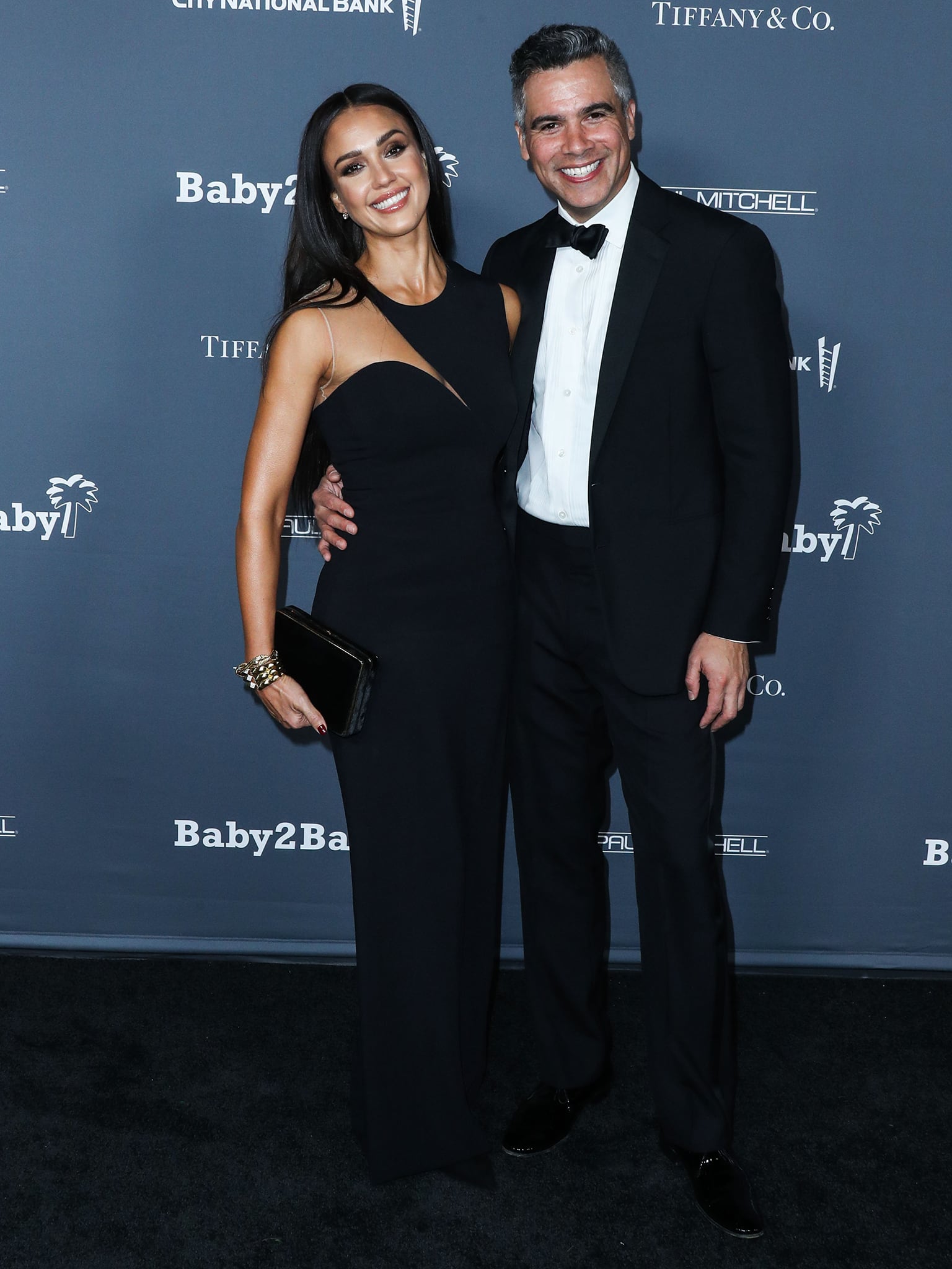 Jessica Alba and Cash Warren share a polished red carpet moment at the Baby2Baby 10th Anniversary Gala on November 13, 2021, with Alba elevating her sleek black gown with barely-there heels and sculptural gold jewelry for a timeless evening look