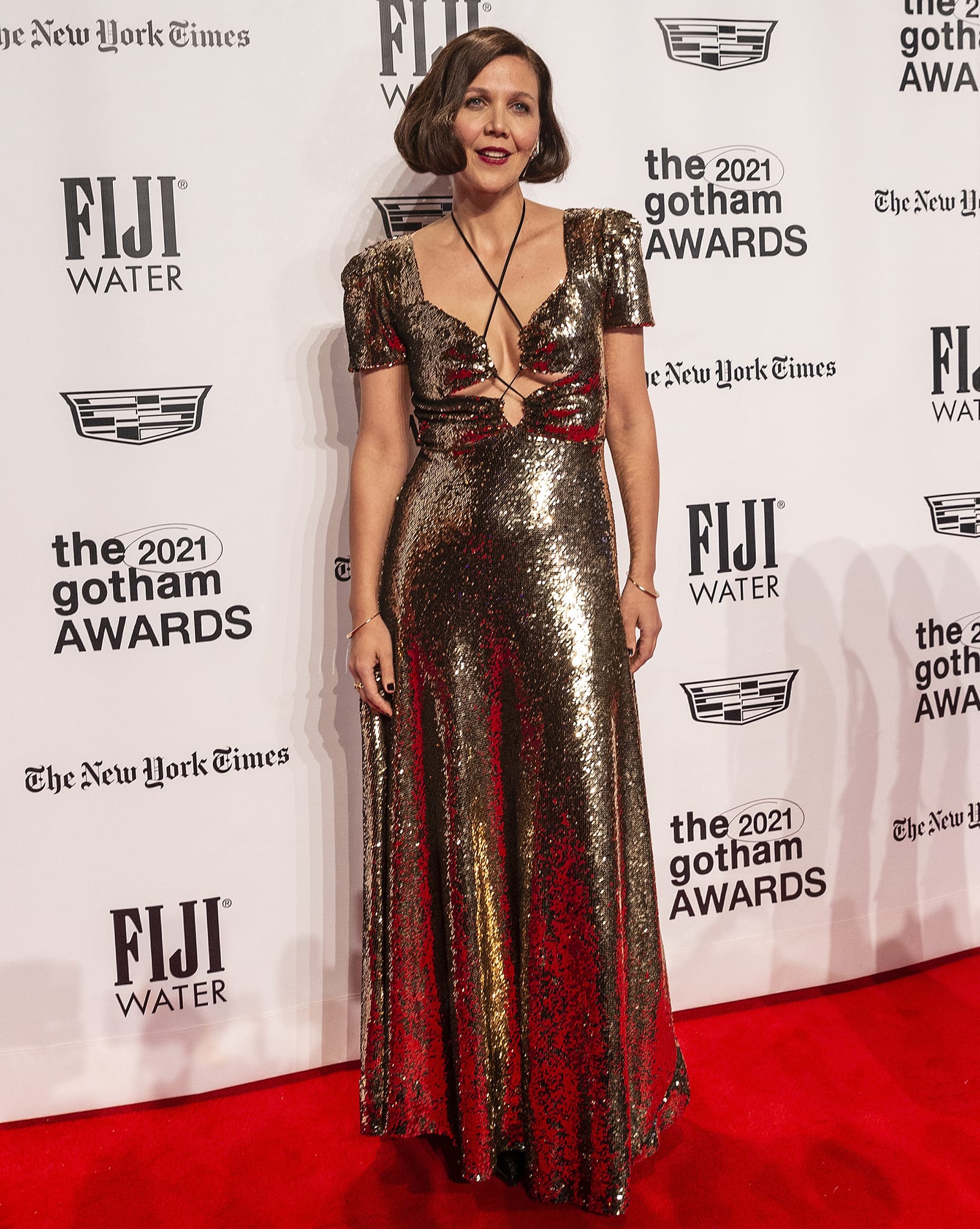 Maggie Gyllenhaal turns heads in a gold sequin Rodarte Fall 2021 gown with a daring cutout bodice, her concealed heels letting the dress’s full shimmer take center stage