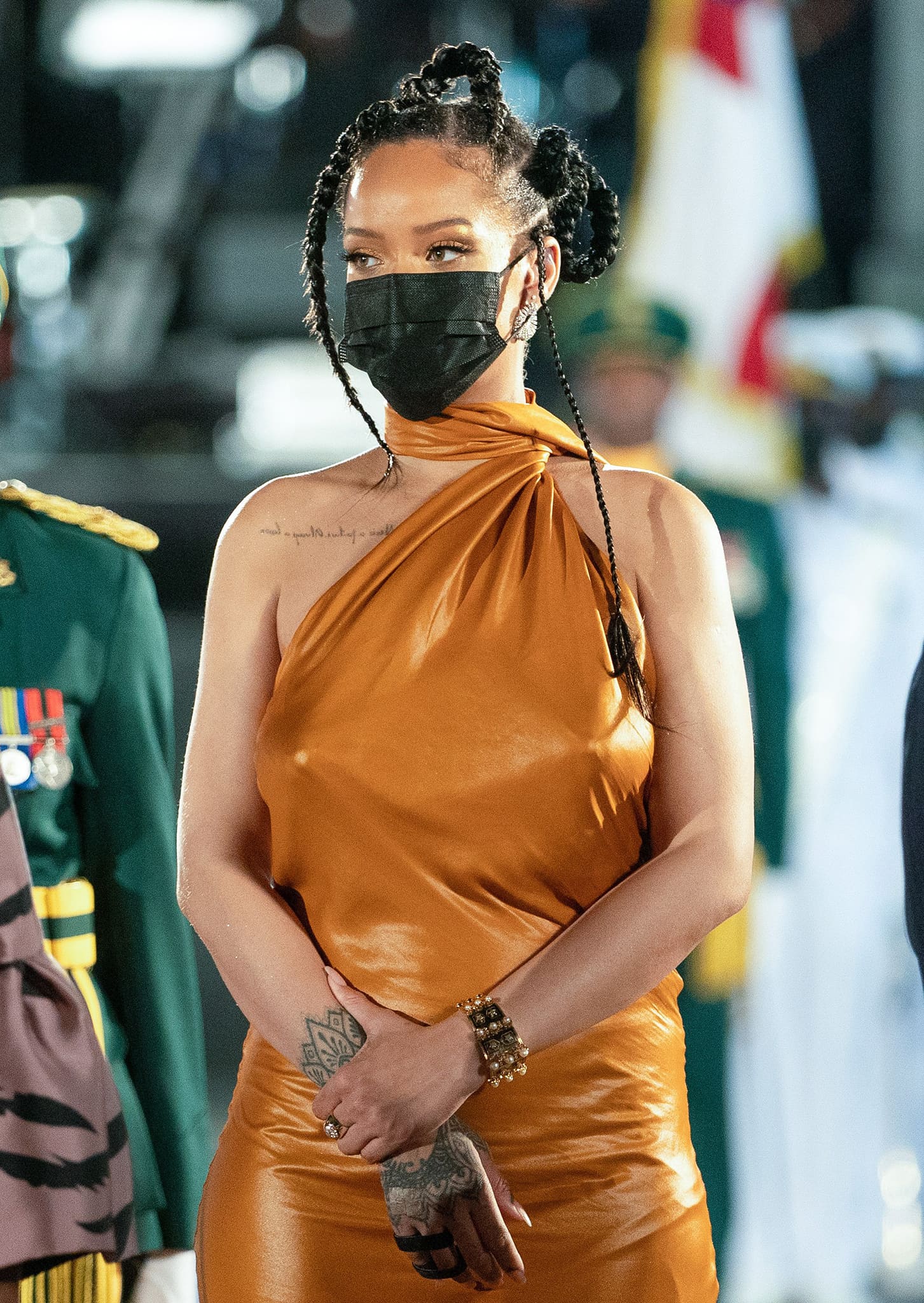 Rihanna accessorized her silky Bottega Veneta gown with statement jewelry, including gold bracelets and rings, showcasing her intricate hand tattoos and chic braided hairstyle