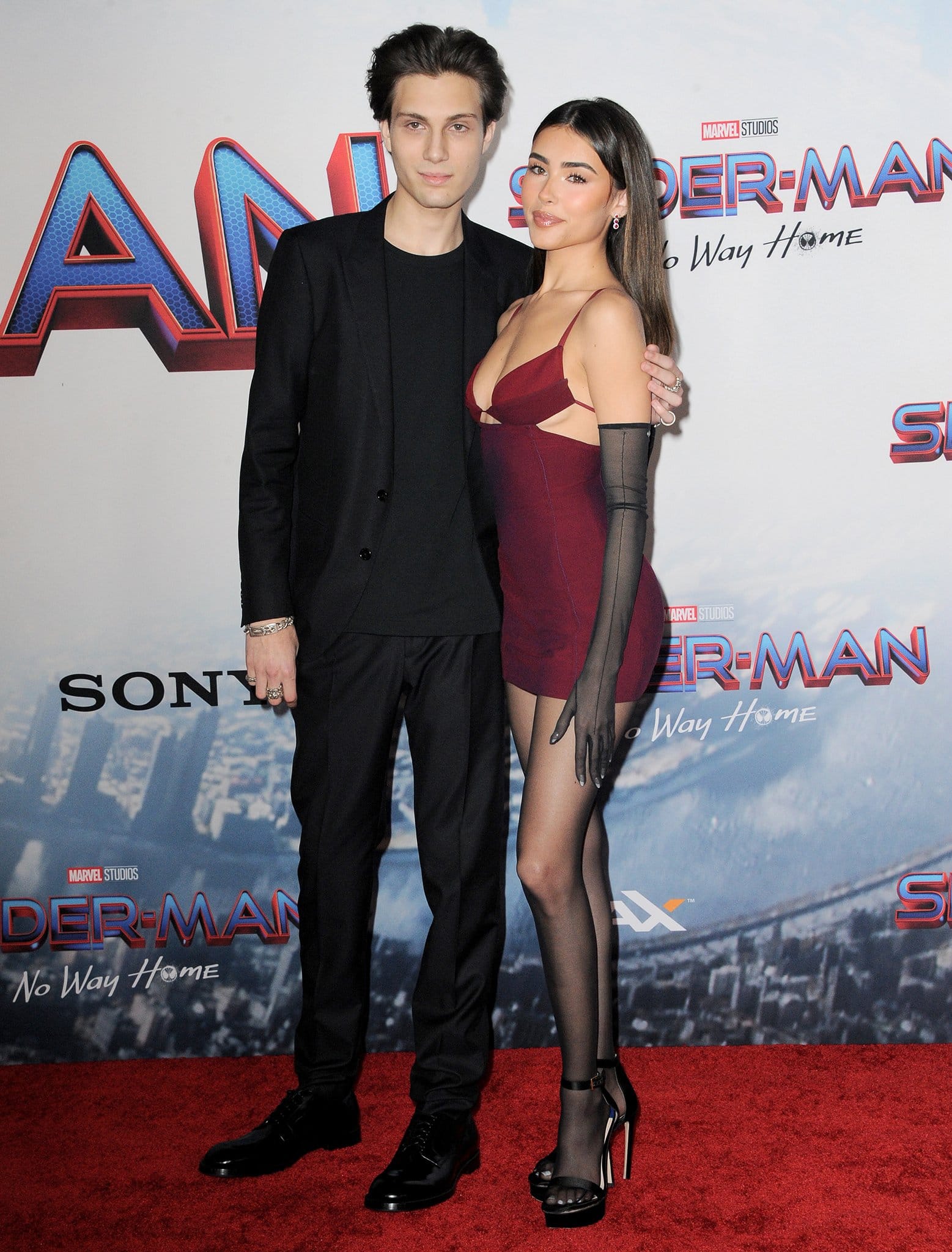 Madison Beer attended the Spider-Man: No Way Home Los Angeles premiere with her younger brother Ryder Beer, styling her burgundy Nensi Dojaka mini dress with sheer gloves, seamed tights, and black Stuart Weitzman platform sandals