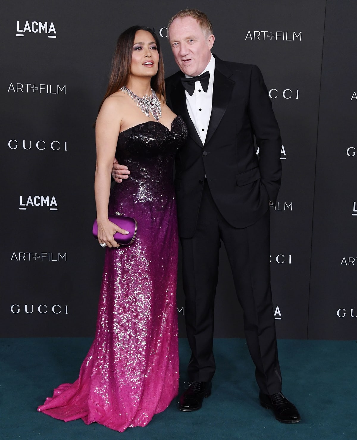 Salma Hayek Pinault shimmers in a strapless, ombré sequined Saint Laurent gown fading from inky black to vivid fuchsia, accessorized with a statement diamond necklace and a purple satin clutch, as she poses with her husband François-Henri Pinault at the 10th Annual LACMA Art+Film Gala