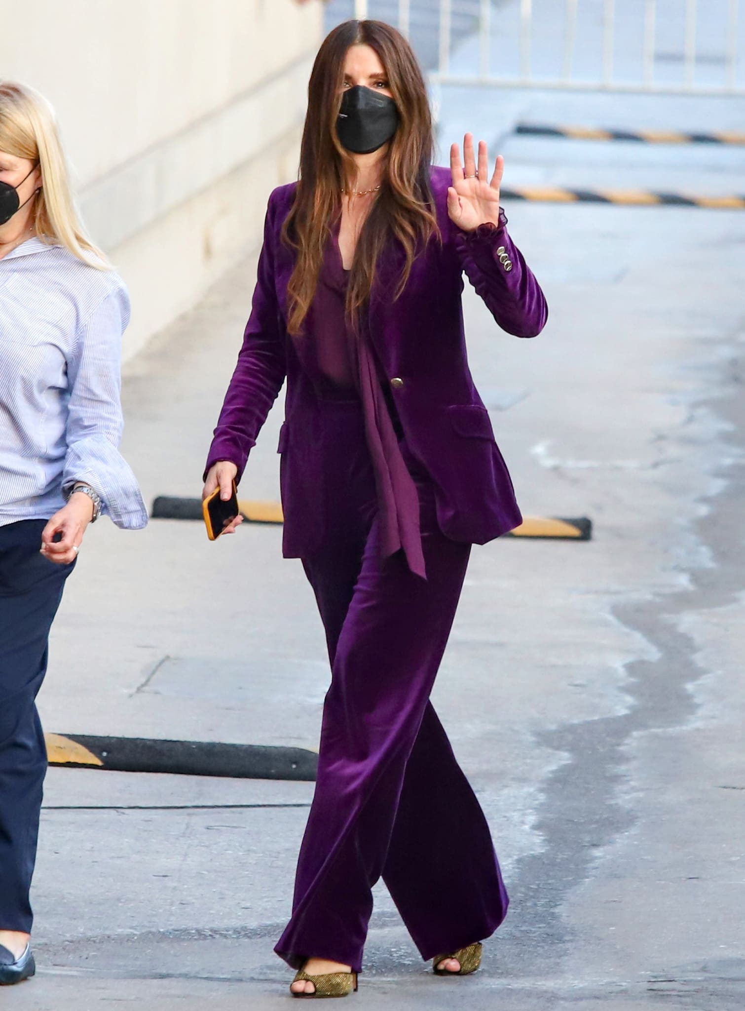 Sandra Bullock pairing a plum Temperley London velvet pantsuit with gold-studded Alexandre Birman “Jenny” sandals