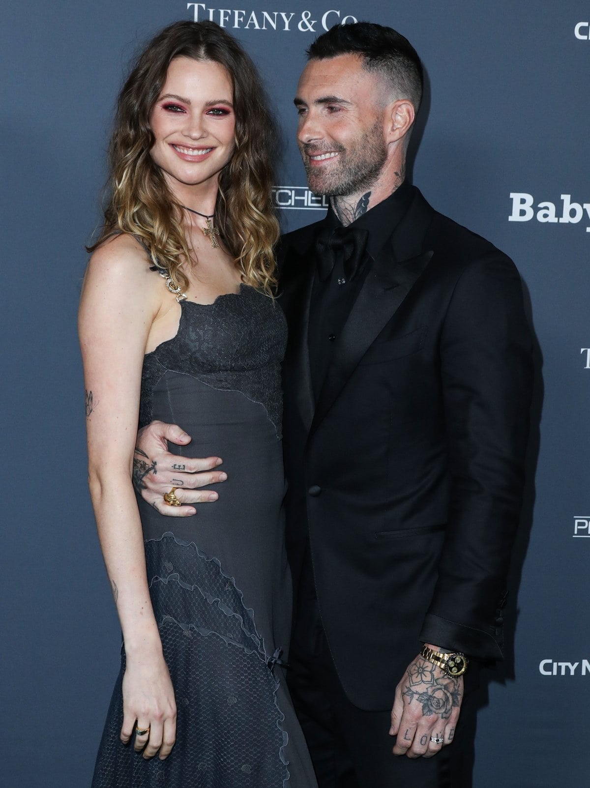 Adam Levine and Behati Prinsloo make a stunning duo on the red carpet, with Adam looking sleek in an all-black suit and Behati radiating elegance in a dark lace gown