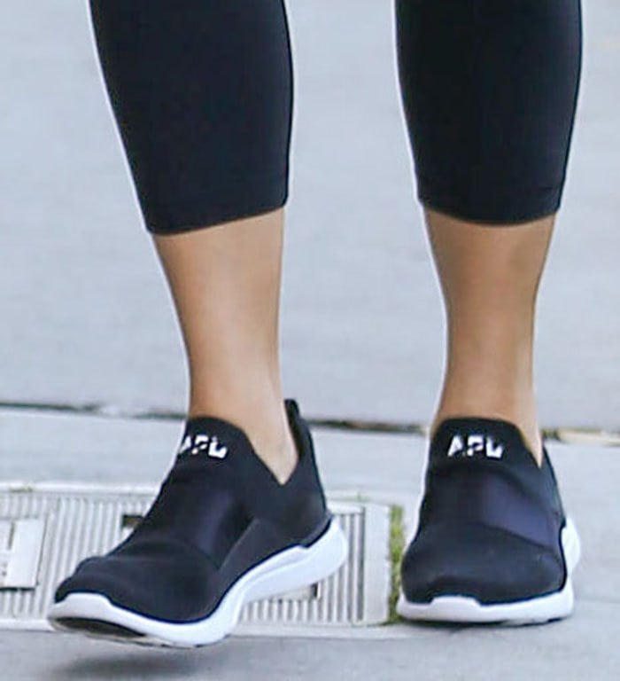 Chrissy Teigen completed her athleisure look with black APL TechLoom Bliss sneakers, pairing the slip-on knit design with cropped leggings for a streamlined off-duty outfit