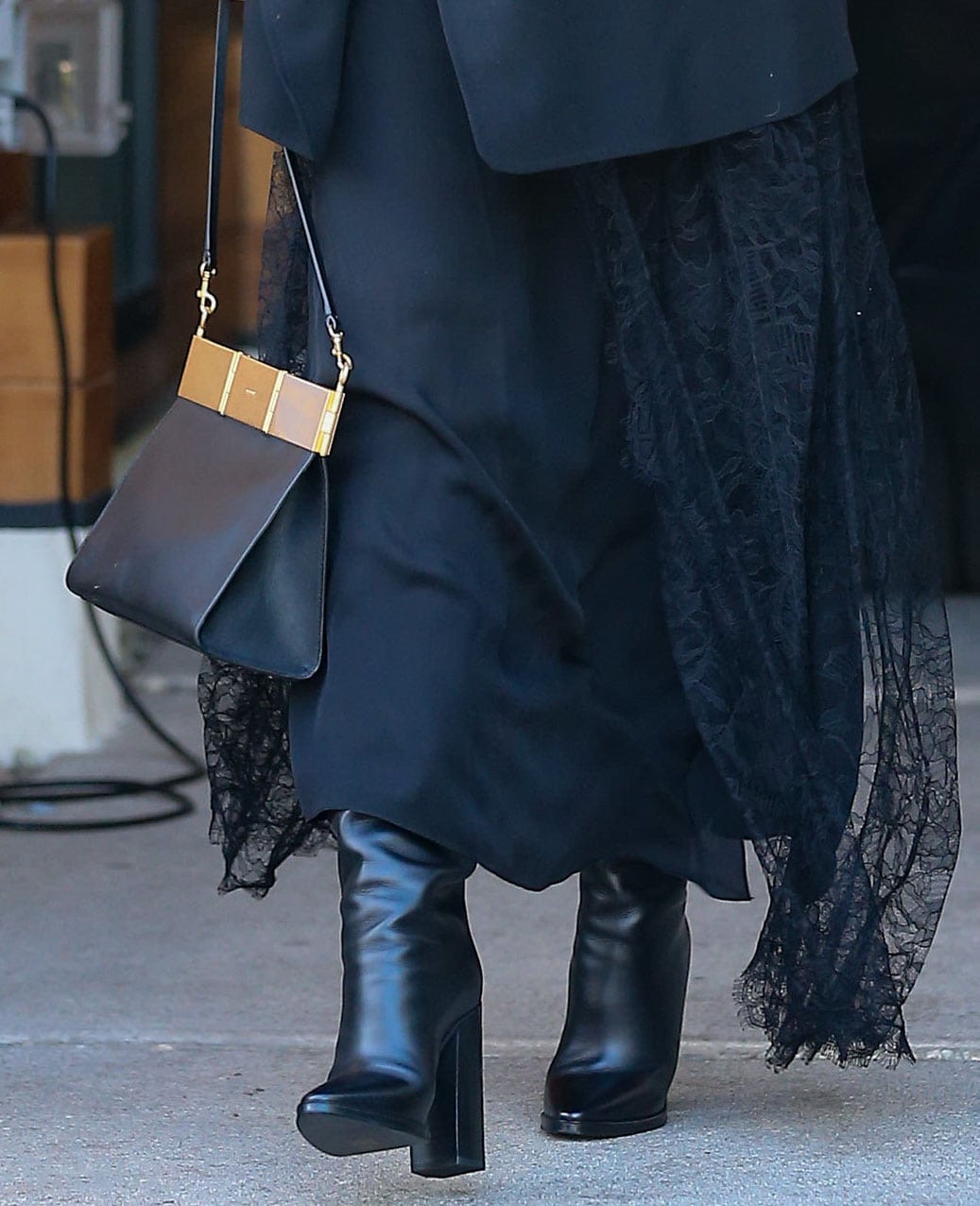Chrissy Teigen pairs her lace maxi dress with Saint Laurent Cleveland knee-high boots, using the sleek leather silhouette and chunky block heels to add modern contrast to the romantic look