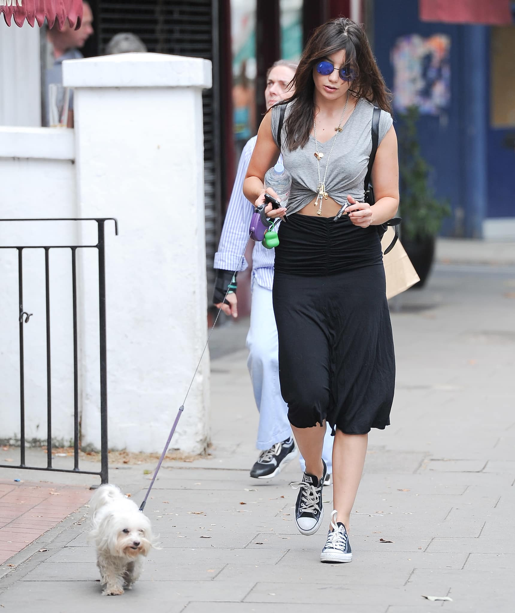 Daisy Lowe keeps things effortlessly cool on a city stroll, pairing classic black low-top Converse sneakers with a ruched midi skirt and a knotted gray tee, while walking her adopted Maltese terrier through the streets of New York