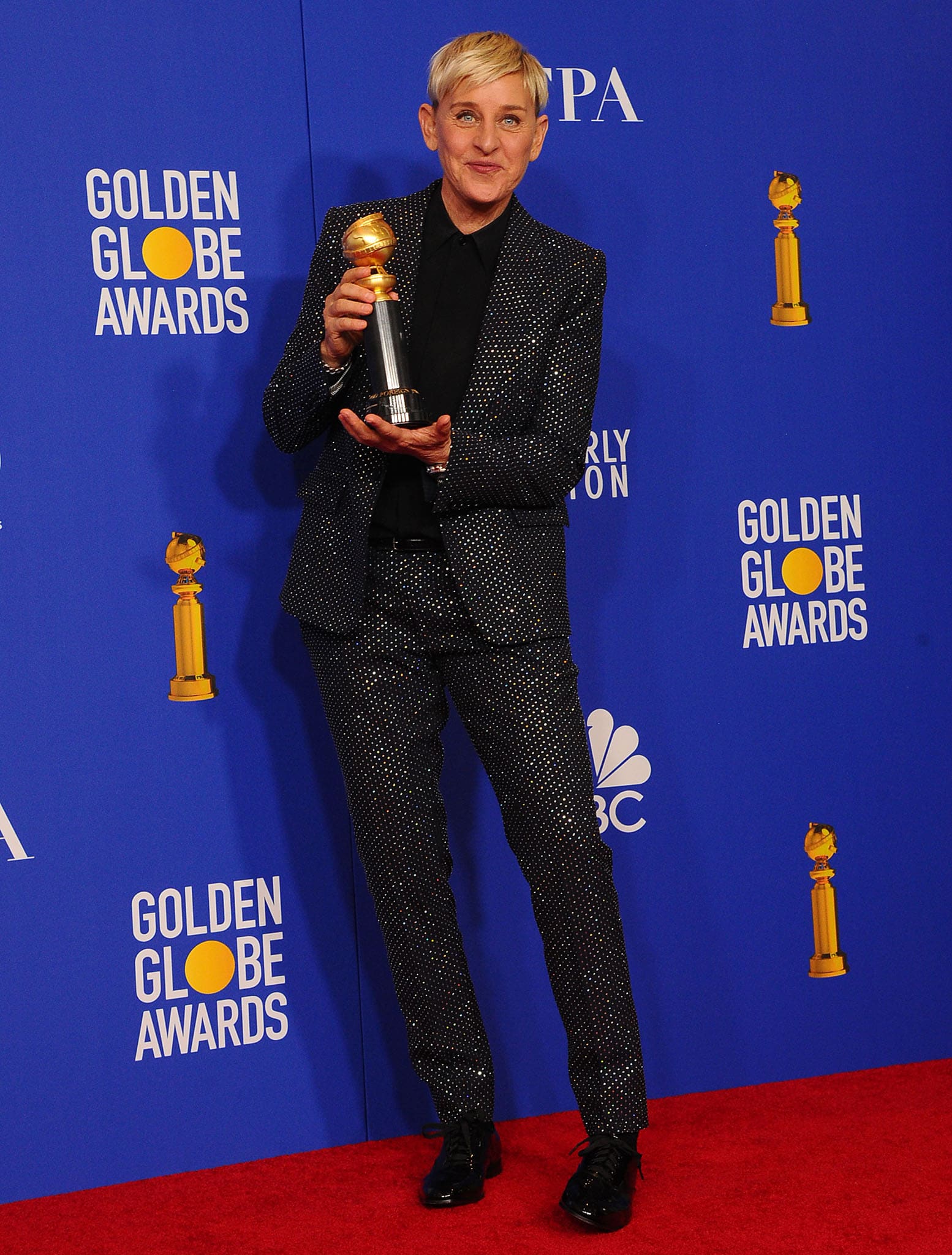 Ellen DeGeneres keeps it classic and cool at the Golden Globe Awards, donning a sparkling black tailored Celine suit paired with shiny black oxford shoes as she proudly holds her trophy