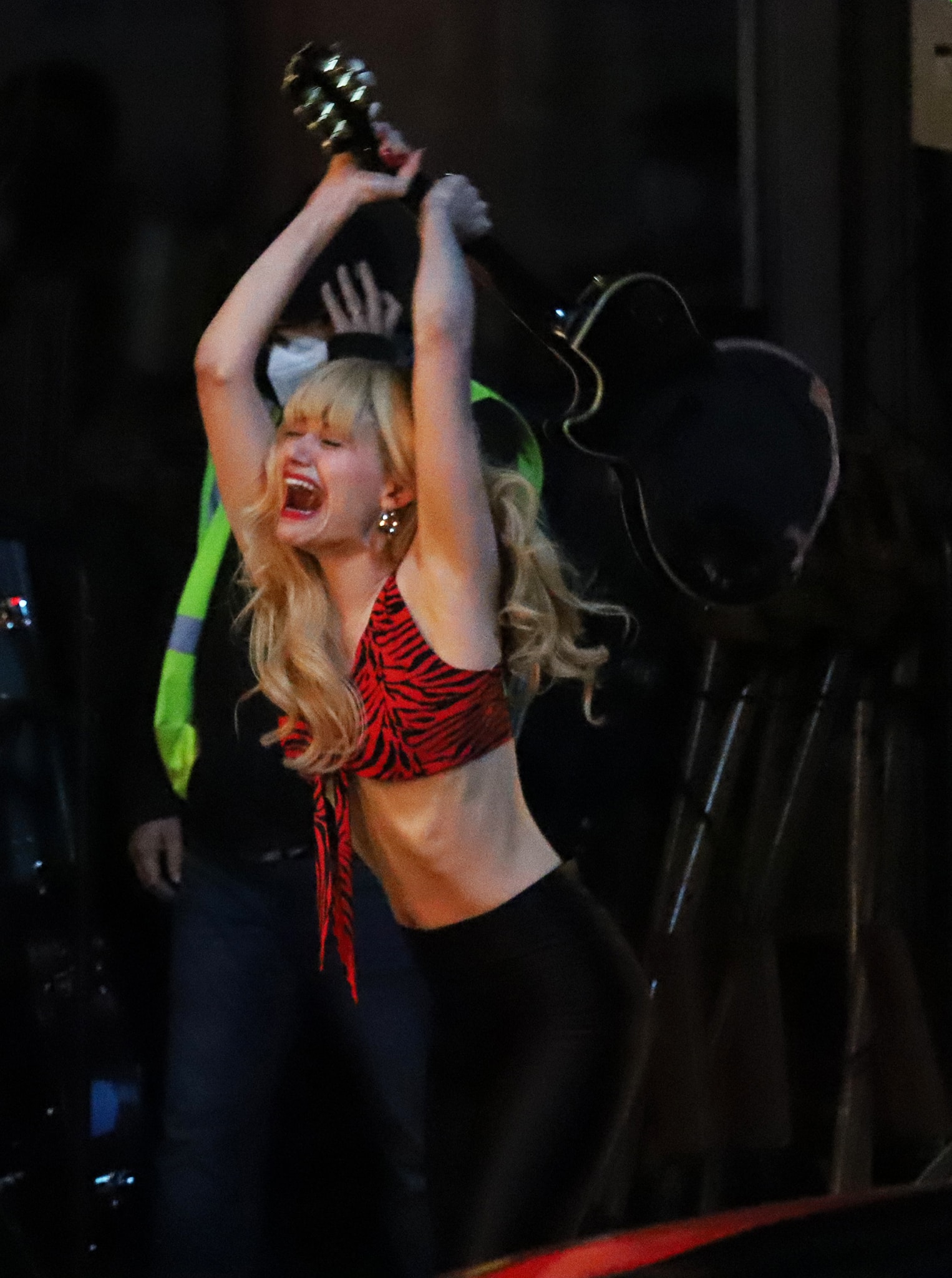 Emmy Rossum leaned fully into Angelyne’s chaotic rock-star energy in a zebra-print crop top and skintight black leggings while filming a dramatic guitar-smashing scene for the Peacock series