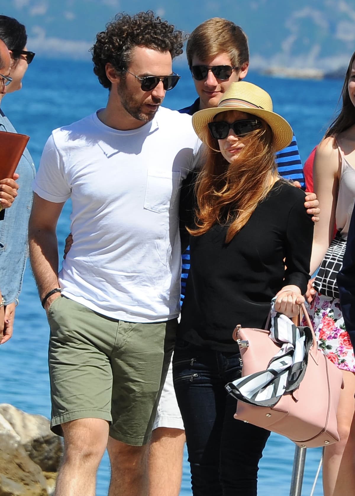 Jessica Chastain enjoyed a relaxed seaside stroll with husband Gian Luca Passi de Preposulo, wearing a black knit top, skinny jeans, straw hat, and oversized sunglasses, accessorized with a blush-pink handbag tied with a striped scarf