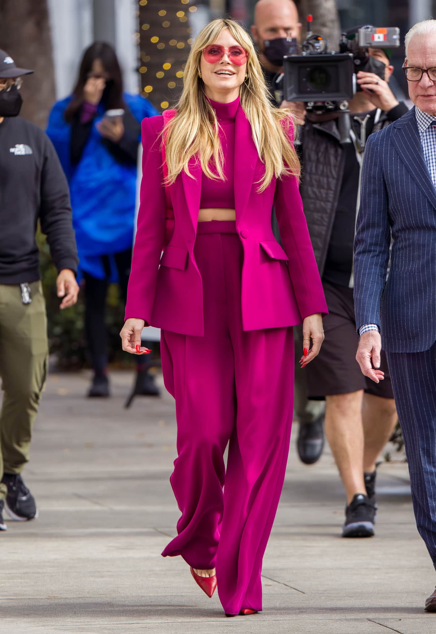 Heidi Klum flashes her abs in a fuchsia pink crop turtleneck top layered underneath a matching fuchsia pantsuit