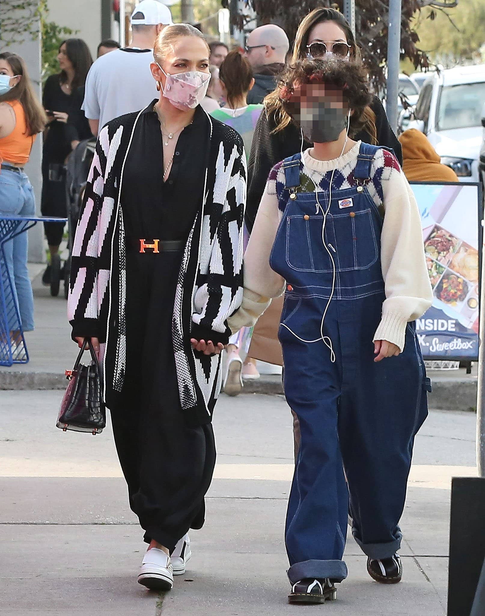 Emme embraces playful, oversized styling in cuffed Dickies denim overalls layered over a cream argyle sweater, finishing the look with black leather lace-up shoes featuring sporty white stripes