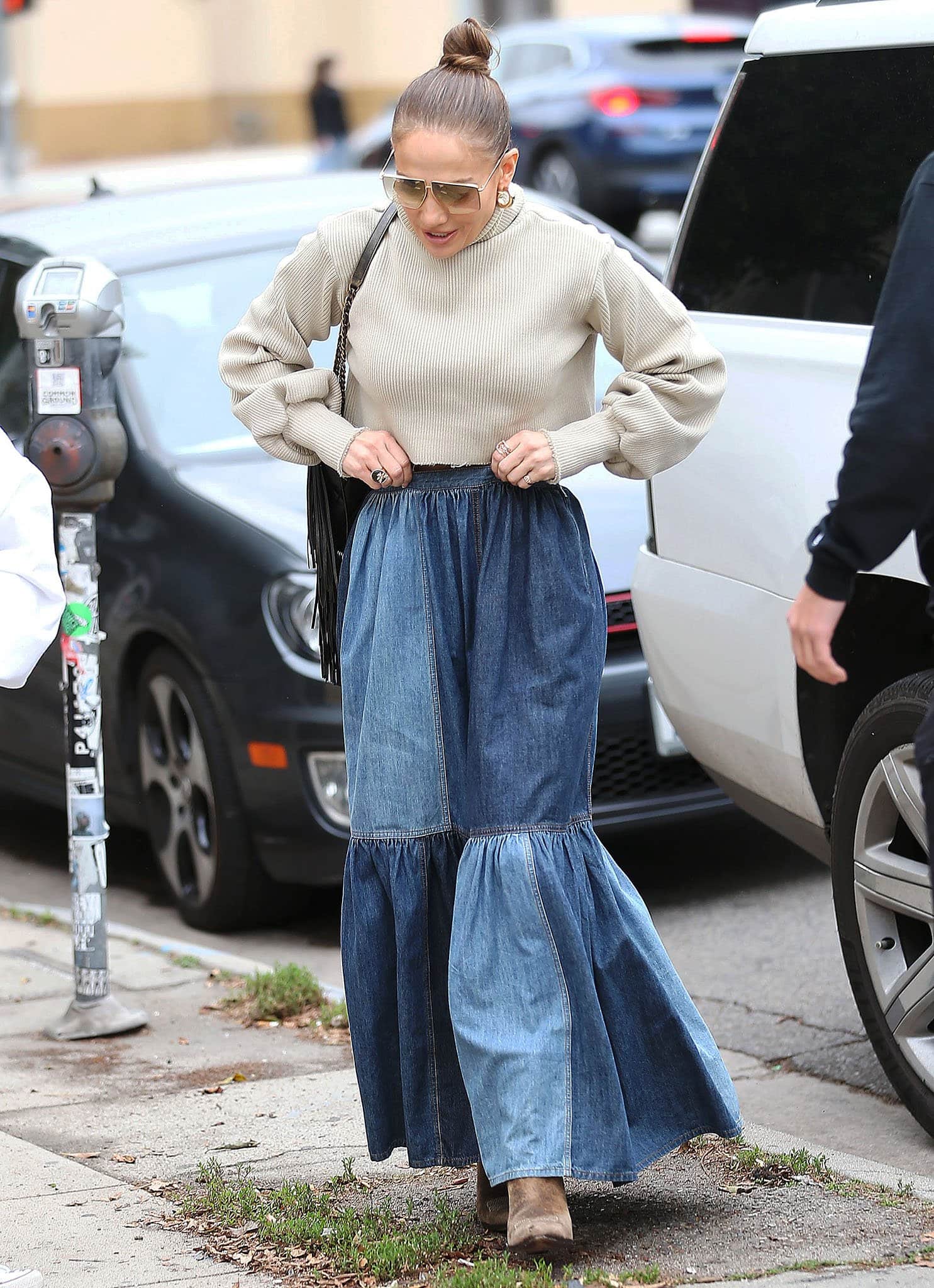 Jennifer Lopez channels relaxed Western glamour in a chunky Orseund Iris knit sweater and flowing patchwork Dior denim maxi skirt, grounding the bohemian silhouette with weathered Ralph Lauren cowboy boots