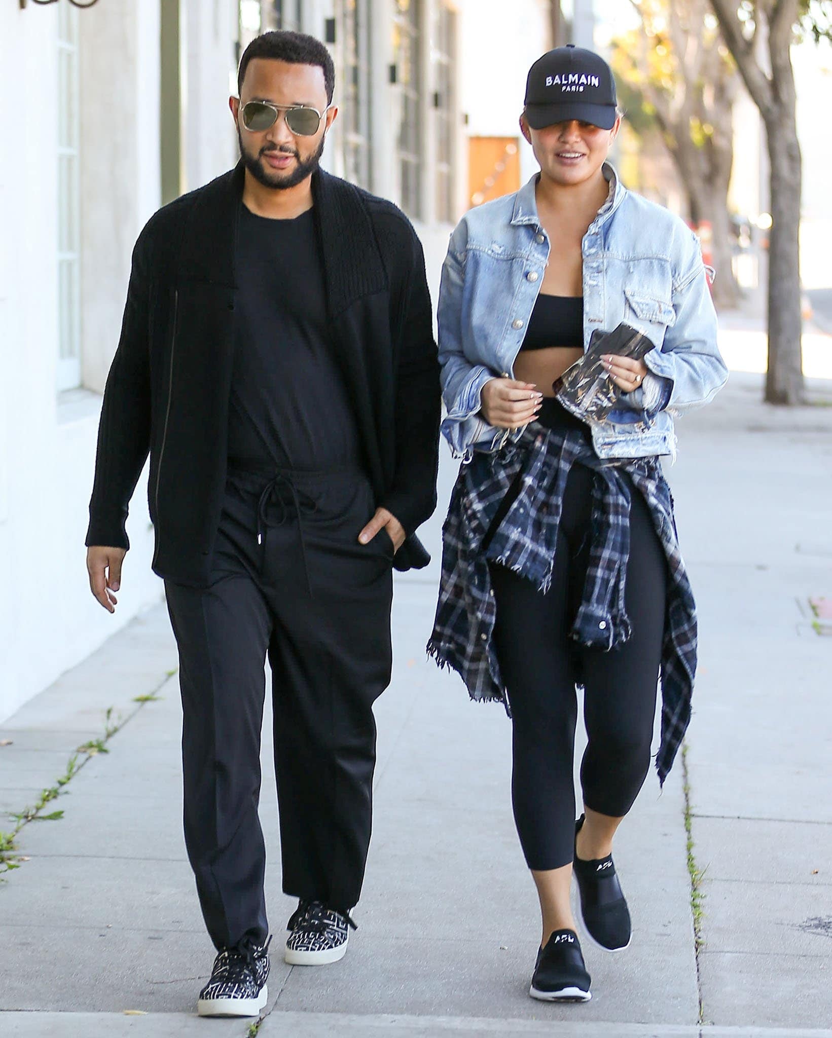 John Legend and Chrissy Teigen stepped out in coordinated off-duty looks in Beverly Hills, pairing Balmain accessories and sneakers with APL TechLoom Bliss trainers, leggings, and layered denim