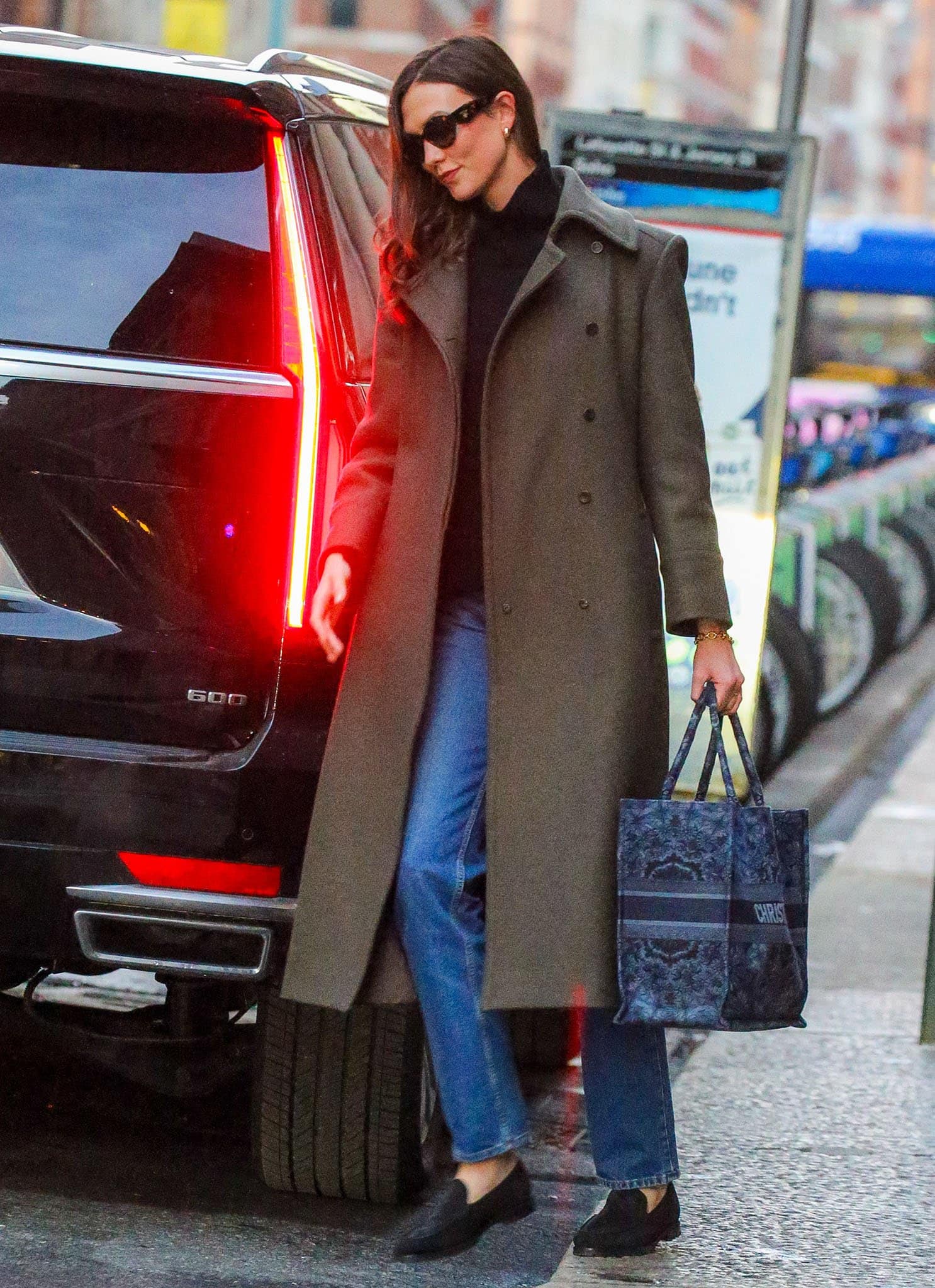 Karlie Kloss balanced practicality and polish with flat black loafers, a sweeping olive coat, and a structured Dior Book Tote while navigating the Manhattan streets
