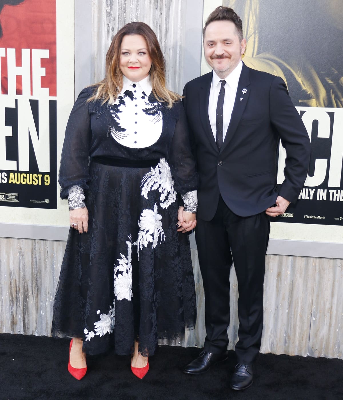 Melissa McCarthy adds a bold pop of color with red pointed-toe pumps, standing beside her taller husband Ben Falcone at the premiere of The Kitchen