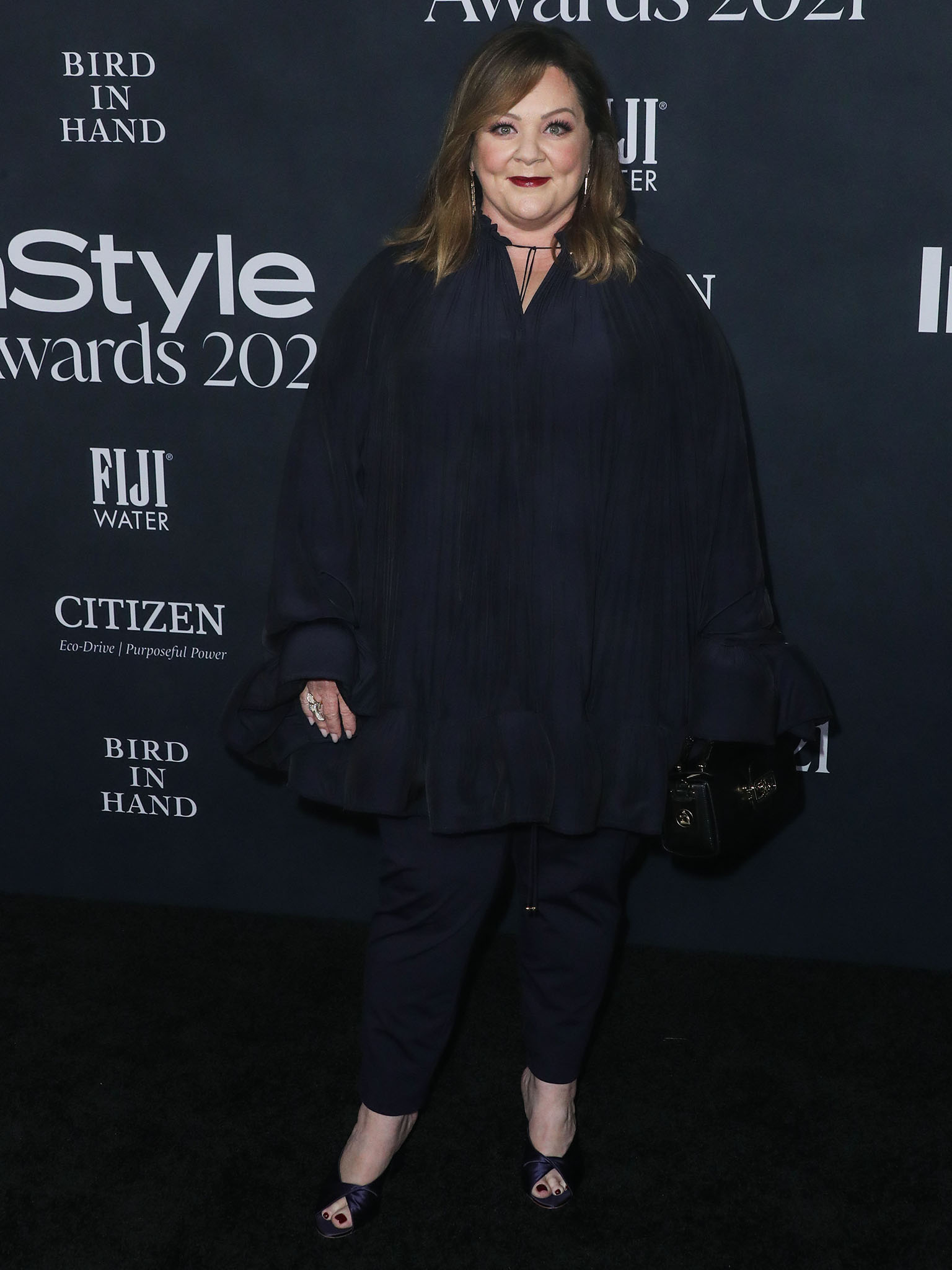 Melissa McCarthy stuns in a voluminous navy ensemble with sheer layers and cropped pants, finishing the look with dark satin peep-toe heels and a bold red lip for a sophisticated touch at the 2021 InStyle Awards