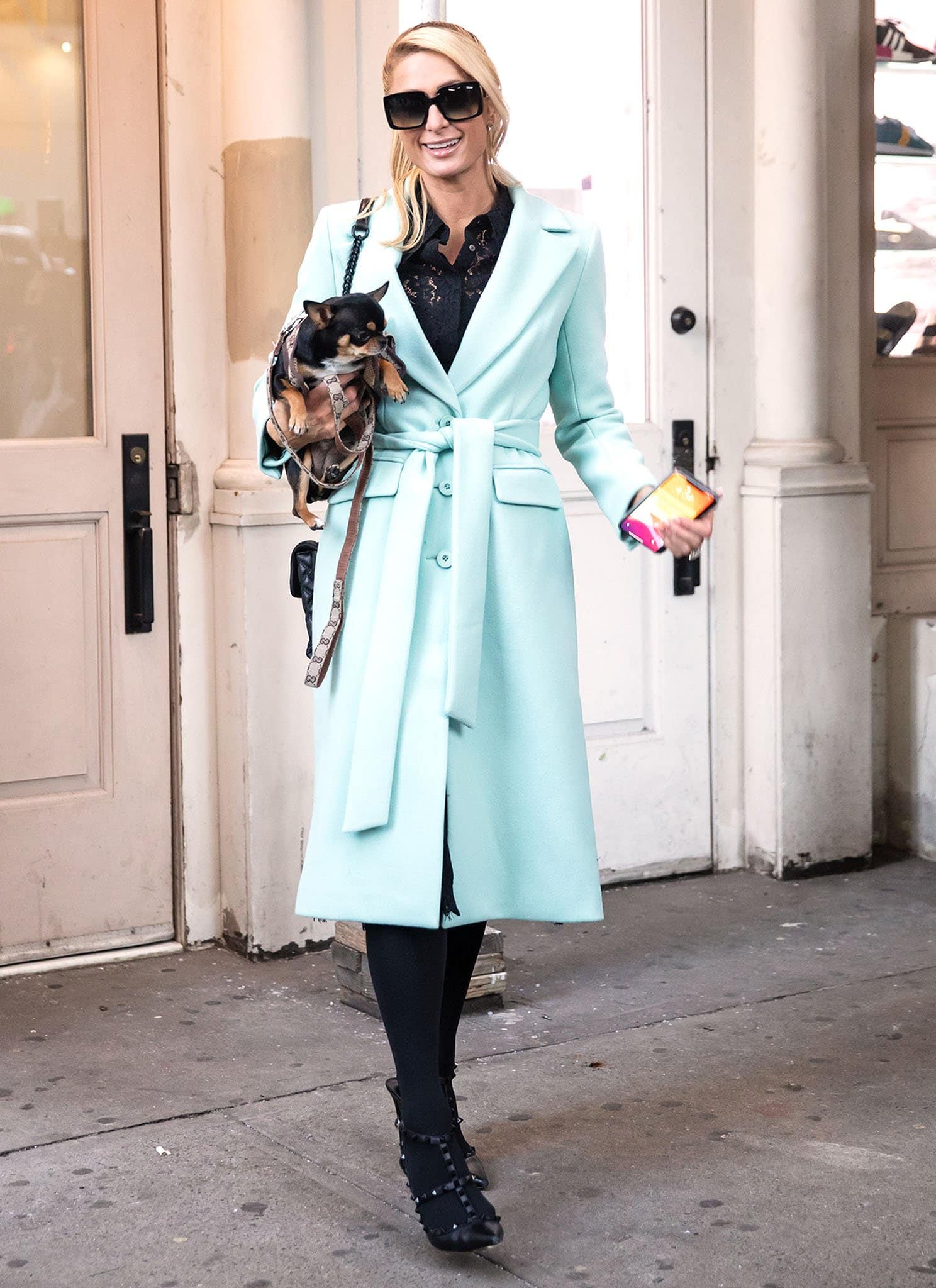 Paris Hilton in a mint wrap coat over a black lace blouse with black tights and Valentino Rockstud pumps