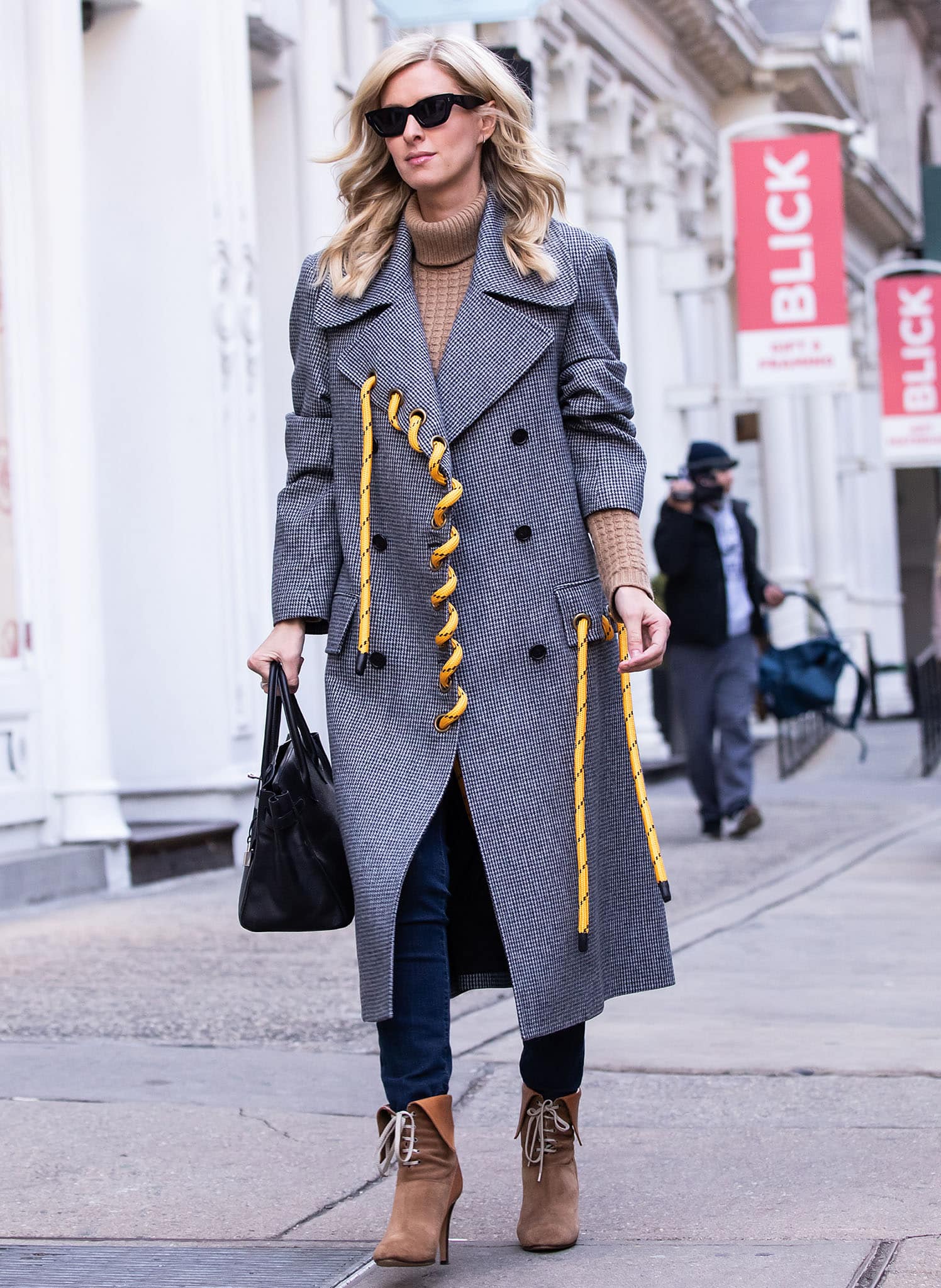 Nicky Hilton layers a tan turtleneck and skinny jeans beneath a Monse houndstooth coat, distinguished by bright yellow rope threaded through oversized brass grommets