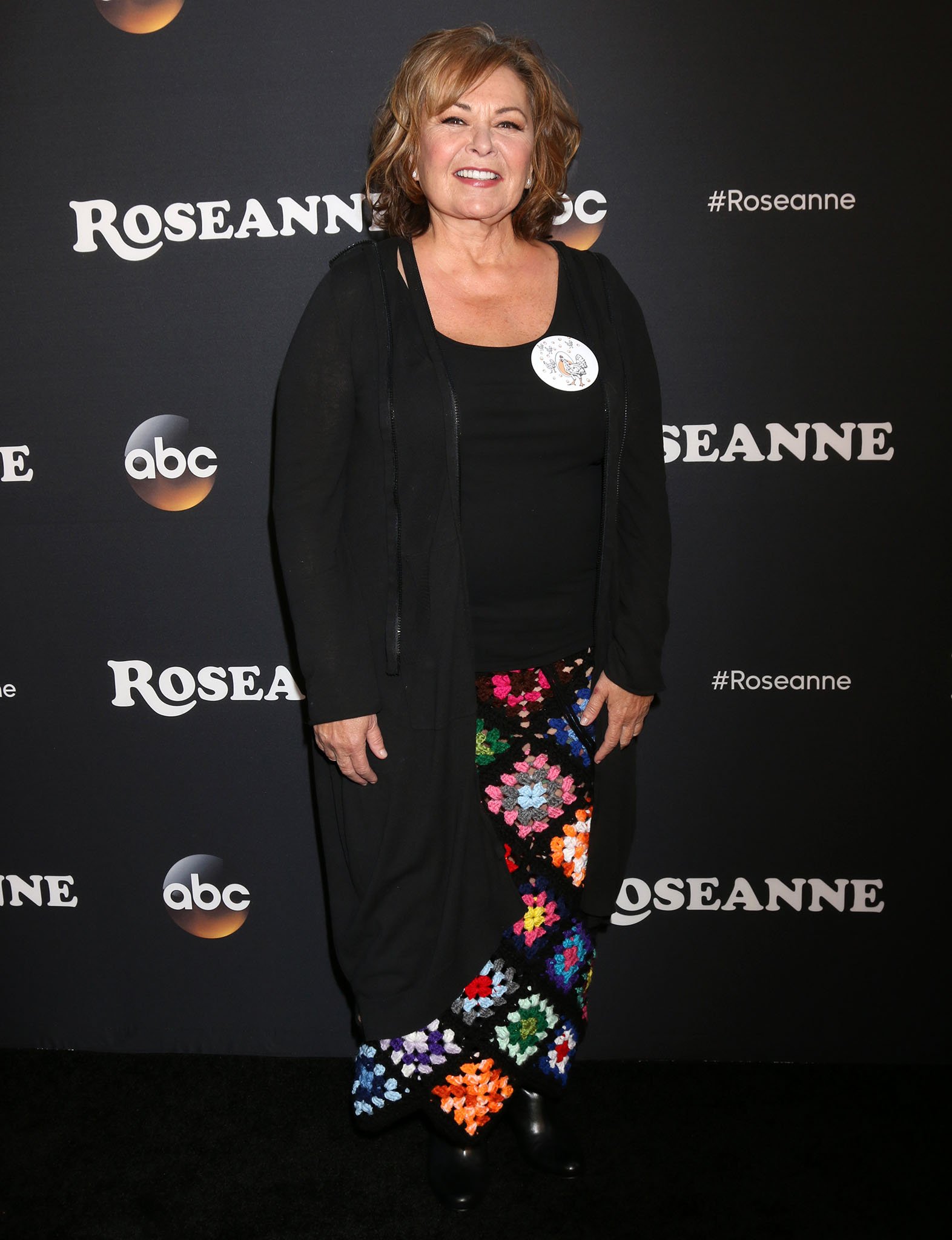 Roseanne Barr adds a splash of retro flair with a colorful granny-square crochet skirt, pairing it with a classic black top, longline hoodie, and sleek black ankle boots for a look that's both cozy and statement-making