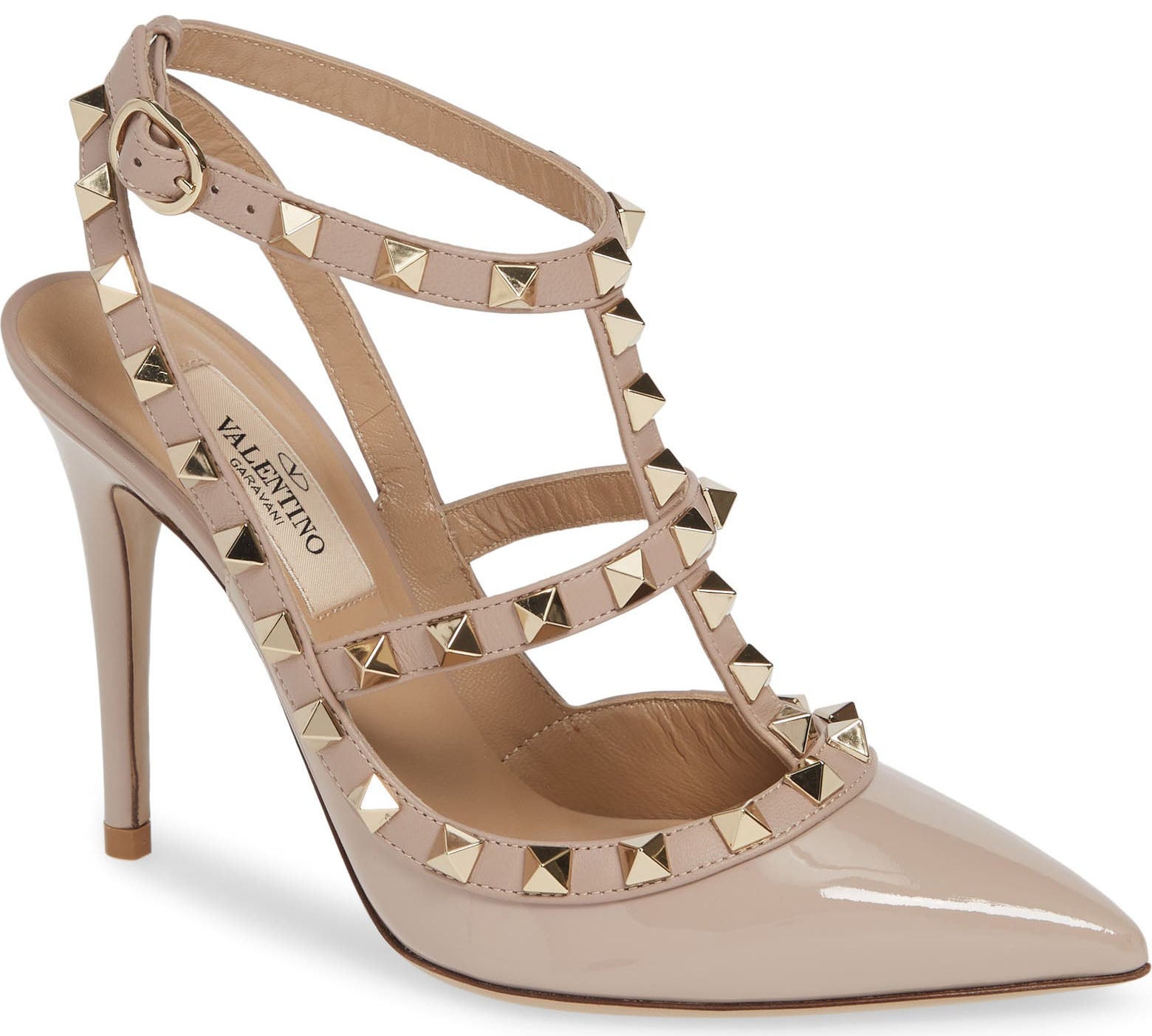 Valentino Garavani Rockstud pumps in Poudre patent leather feature a sharply pointed toe, signature pyramid-studded caged straps, adjustable ankle fastening, and a slender 100mm stiletto heel
