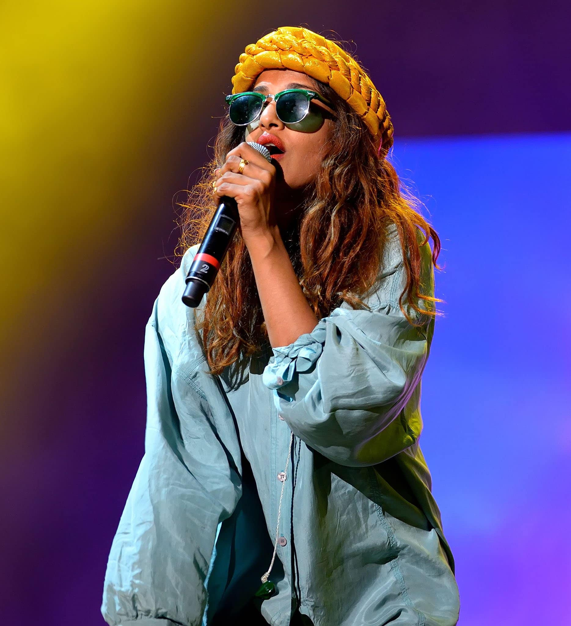 M.I.A. brought effortless cool to the stage in an oversized teal button-up shirt, round green-tinted sunglasses, and a vibrant braided yellow headpiece, blending laid-back style with bold visual flair