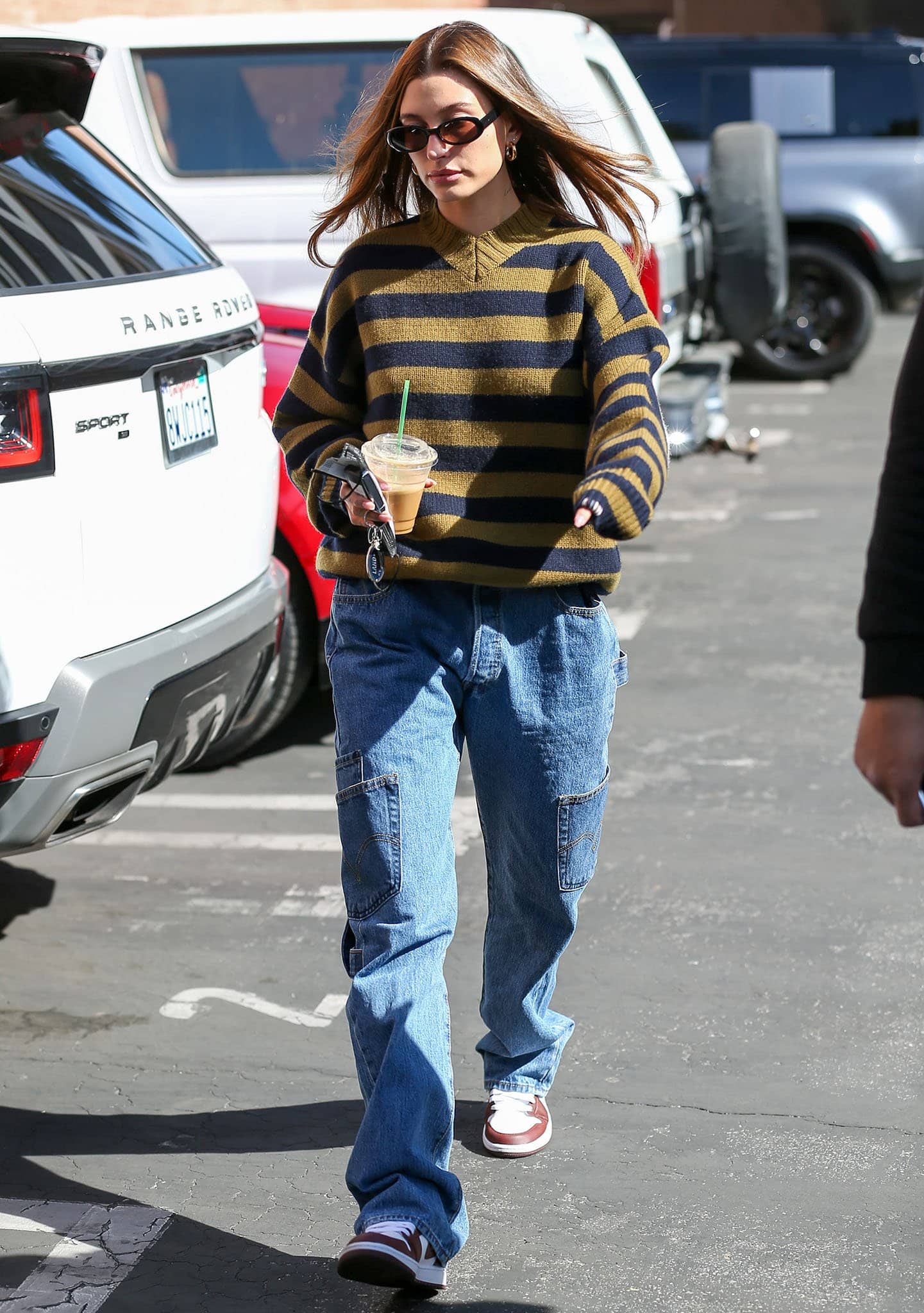 Hailey Bieber runs errands in Los Angeles wearing an Extreme Cashmere striped sweater, Maryam Nassir Zadeh cargo jeans, Dmy by Dmy Valentina sunglasses, and Nike Air Jordan 1 Low "Team Red" sneakers