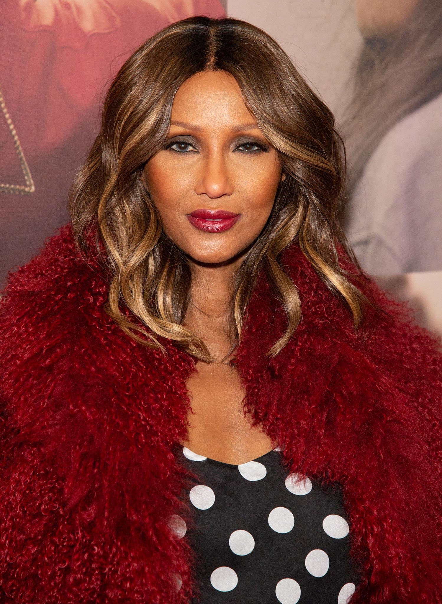 Iman, standing at 5ft 8½ (174 cm), stuns in a bold burgundy fur coat layered over a classic black-and-white polka dot top, exuding timeless glamour and elegance