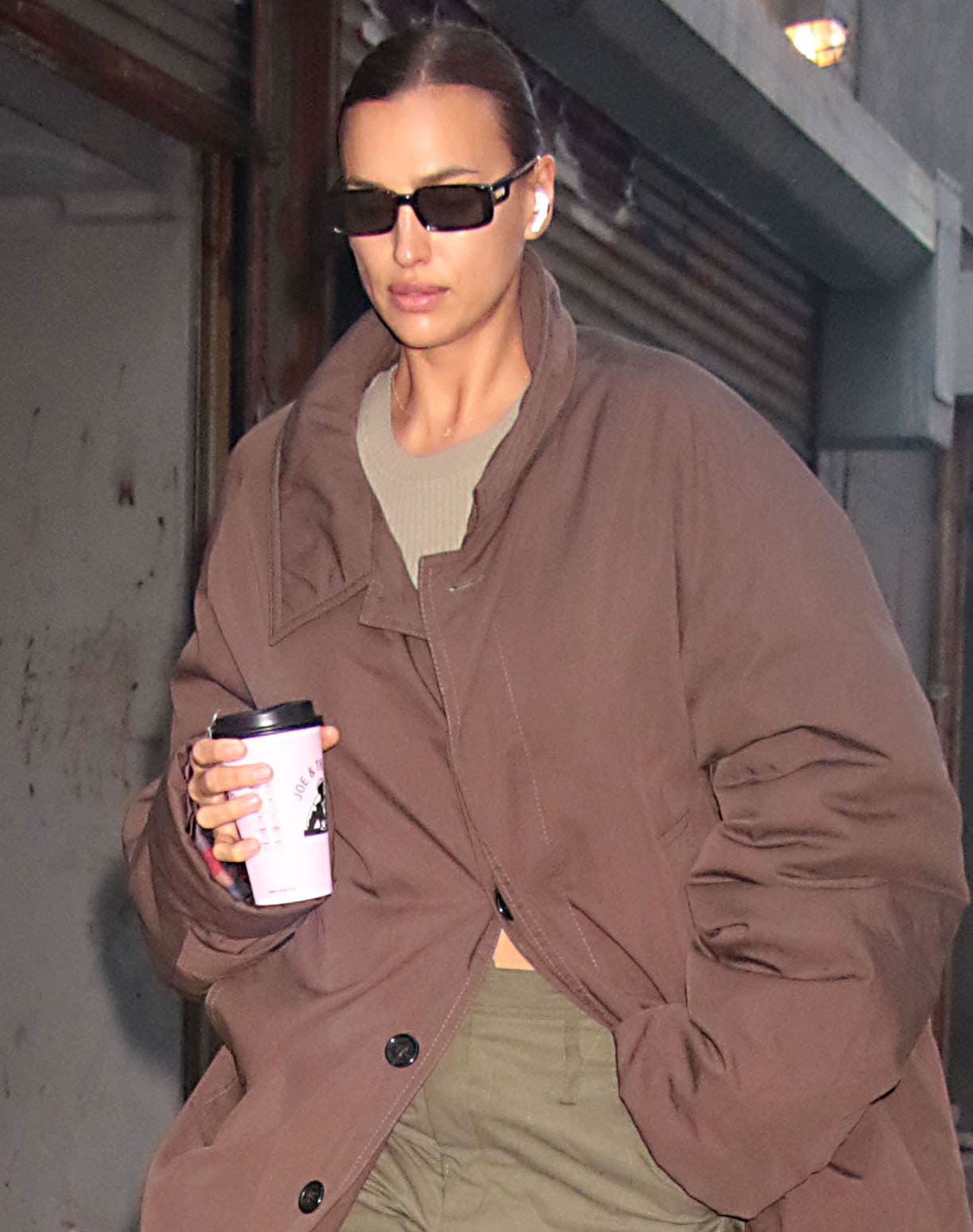 Irina Shayk wears rectangular black sunglasses, a sleek ponytail, and an oversized brown coat in New York City