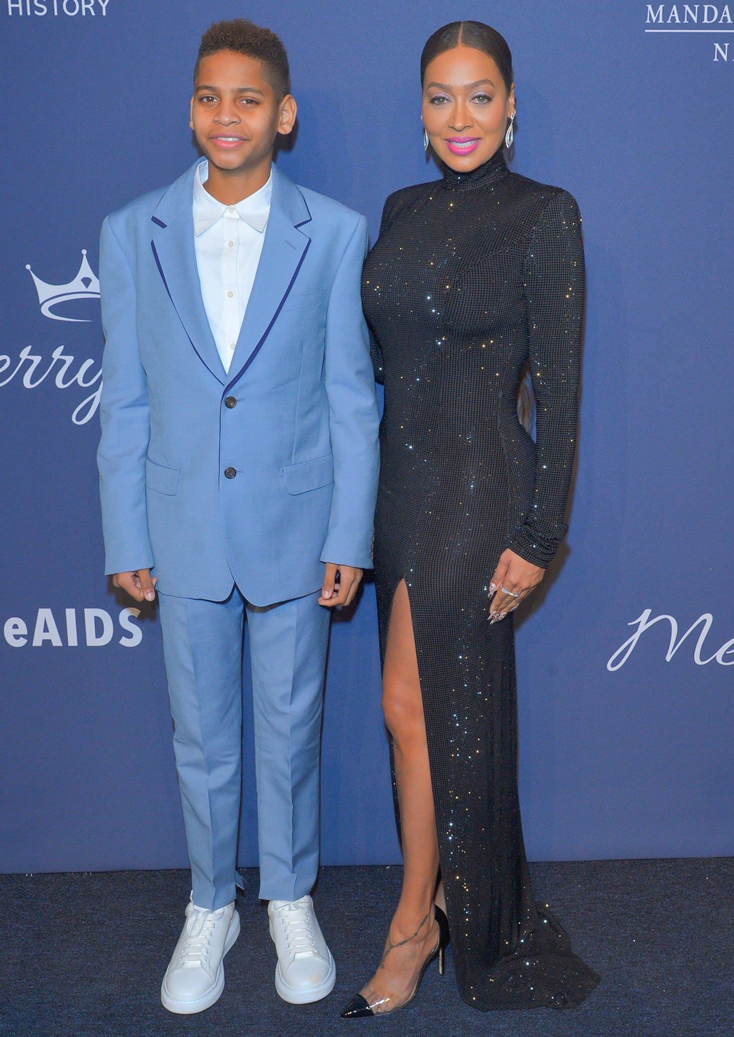 La La Anthony dazzles in a glittering black slit gown and clear-paneled stiletto pumps as her son Kiyan Carmelo Anthony complements her elegance in a crisp powder blue suit and white sneakers