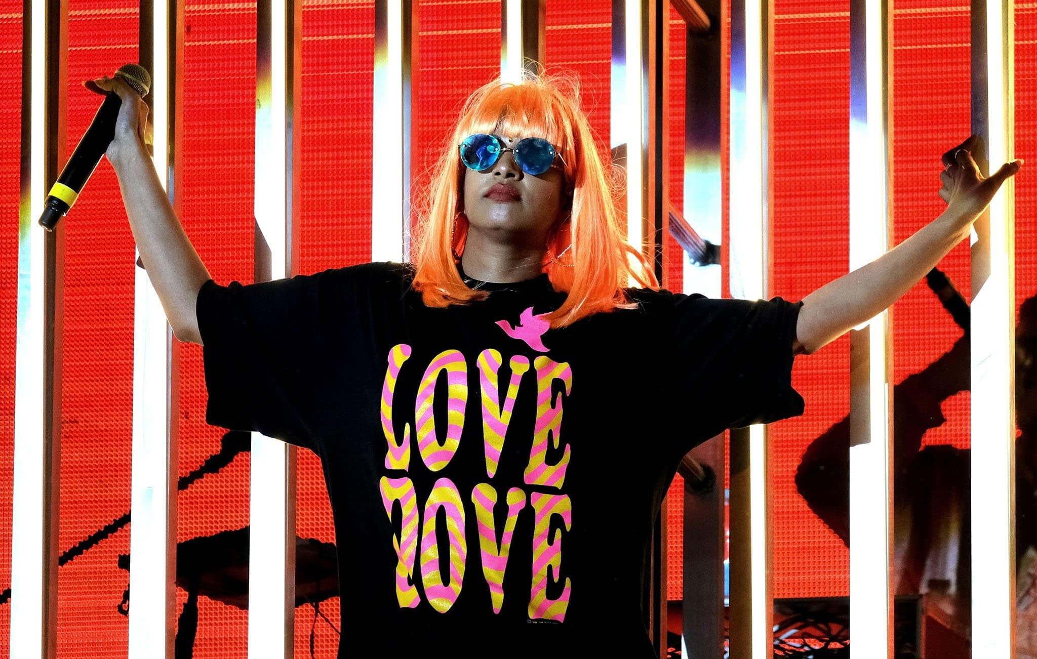 M.I.A. lit up the stage in a bold orange wig, mirrored sunglasses, and an oversized black tee printed with “LOVE LOVE,” delivering her signature mix of rebellious style and electrifying energy