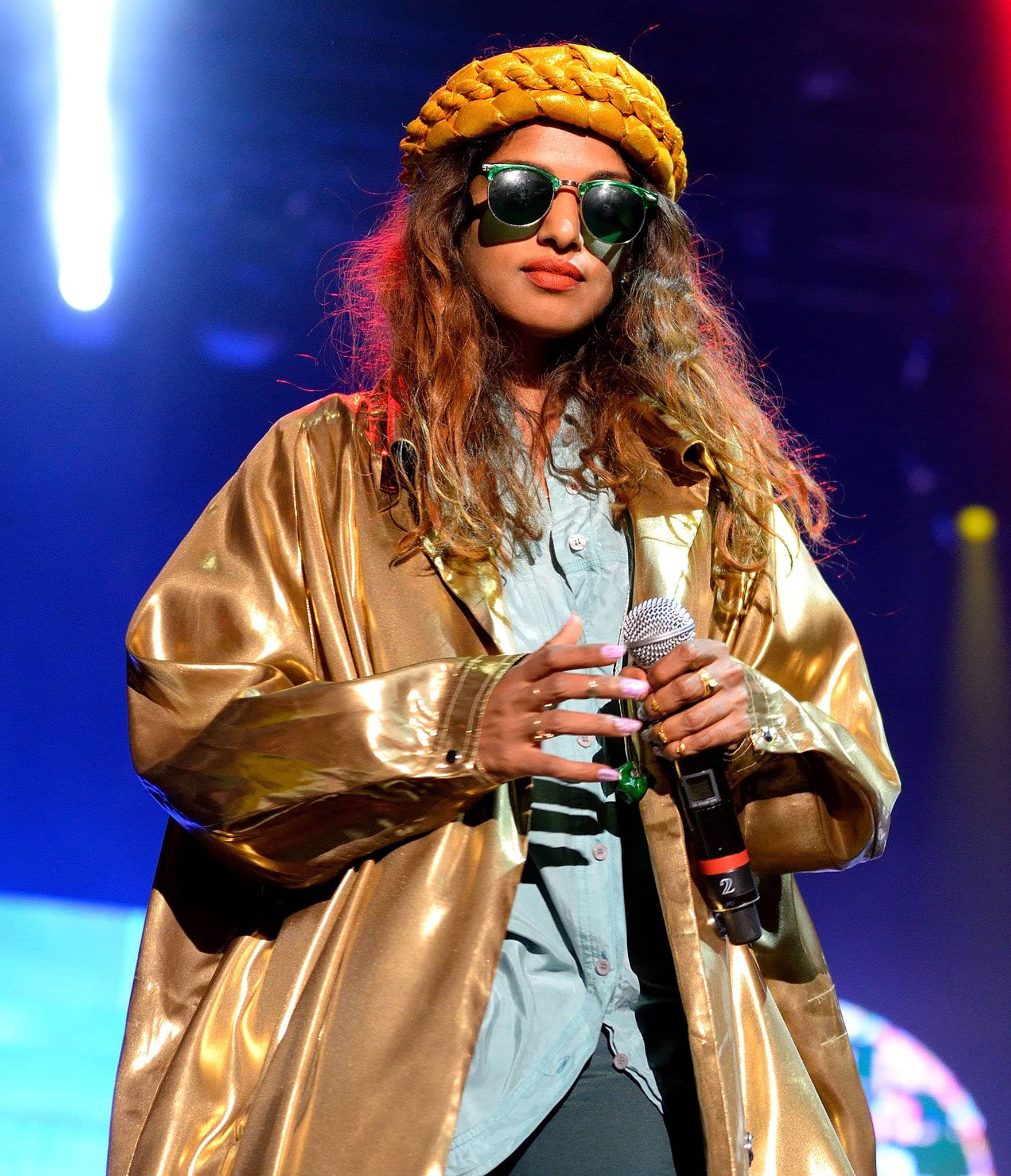 M.I.A. amped up her eclectic stage style with a metallic gold coat layered over a mint button-down shirt, topping off the look with statement green sunglasses and a bold braided yellow headpiece