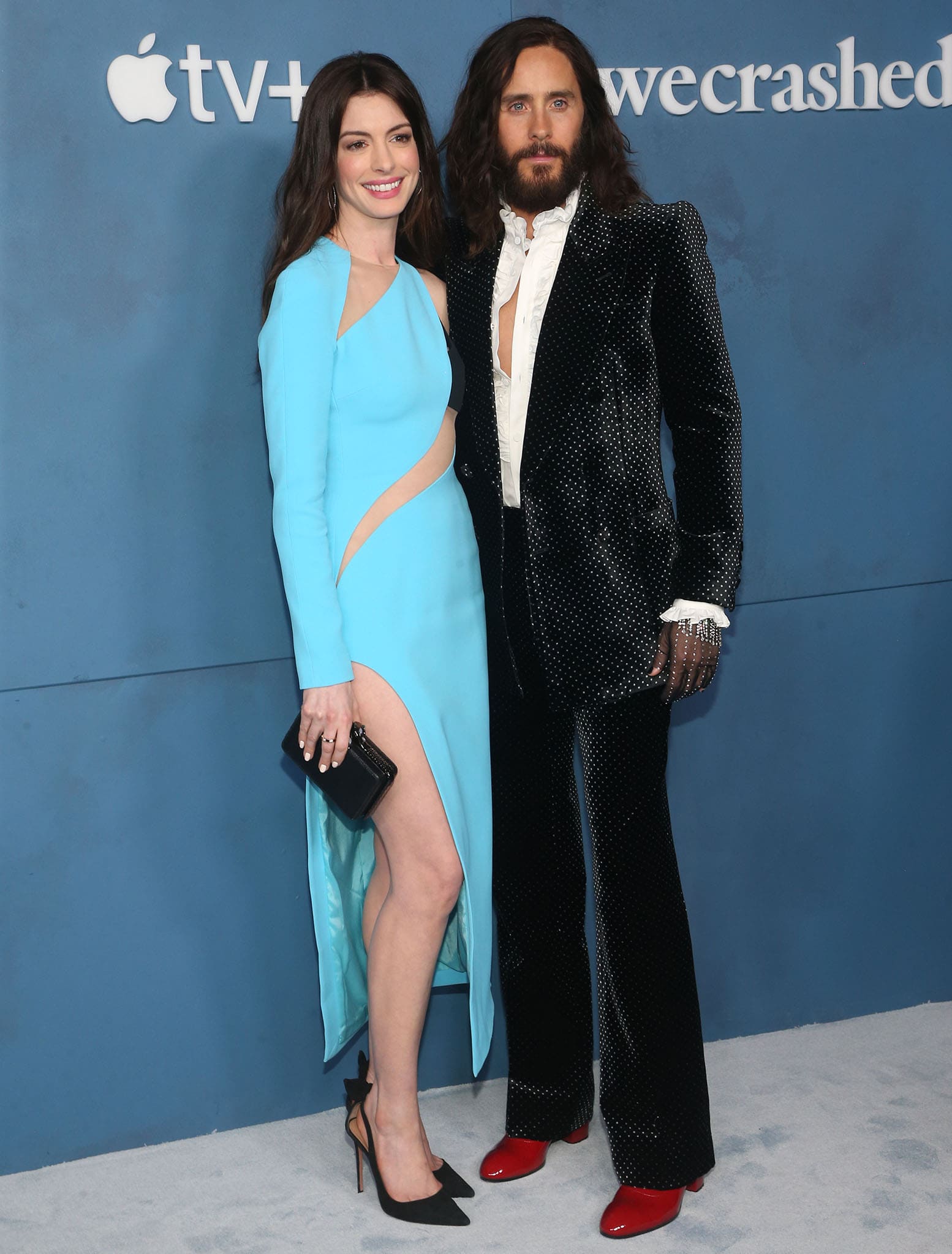 Anne Hathaway commands attention in an aqua David Koma cutout dress styled with black Aquazzura “Bow Tie” pumps, standing alongside Jared Leto in a crystal-studded Gucci suit and bold red boots