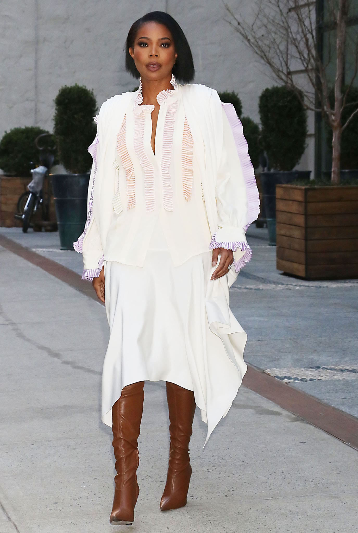 Gabrielle Union leaves The View in a flowing white dress with pleated trims, styled with sharp brown leather knee-high boots featuring pointed toes and high heels