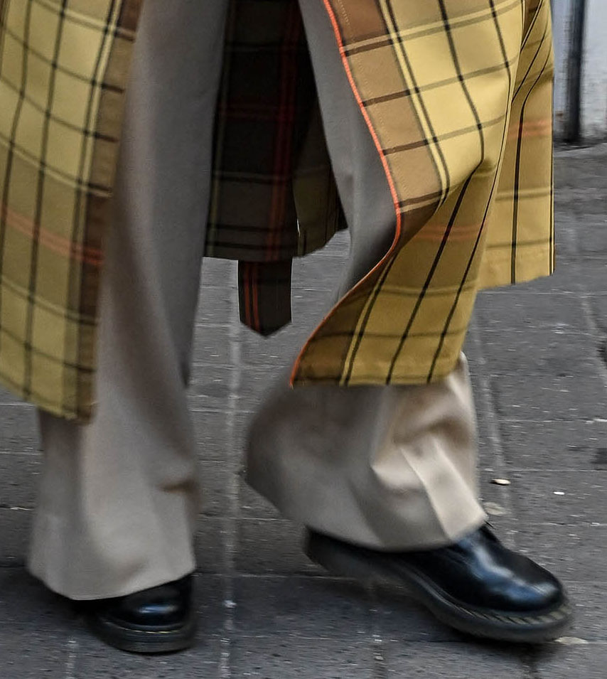 Gigi Hadid grounded her oversized plaid layers with classic black Dr. Martens 1460 boots, adding a utilitarian edge to her relaxed Paris Fashion Week street style look