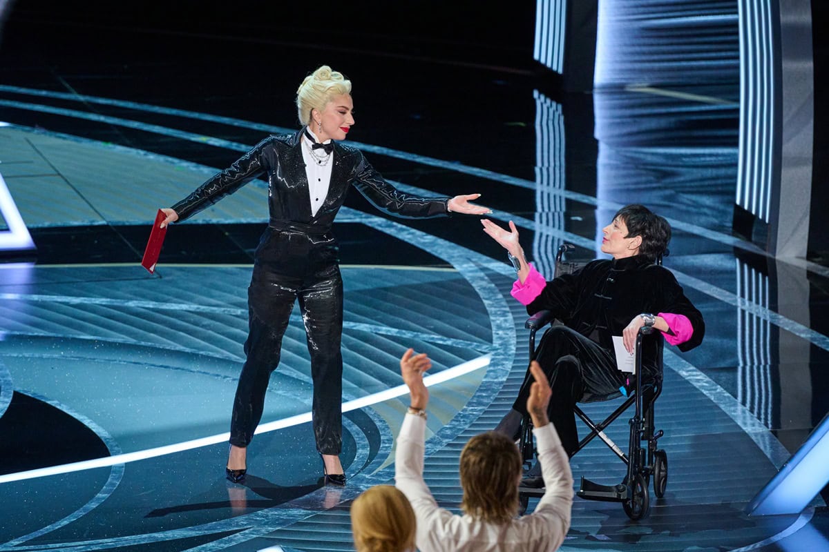 Lady Gaga joins Liza Minnelli onstage at the Oscars to present Best Picture, wearing a Ralph Lauren liquid lamé tuxedo jumpsuit with Jimmy Choo Romy heels and Tiffany Co. diamond jewelry