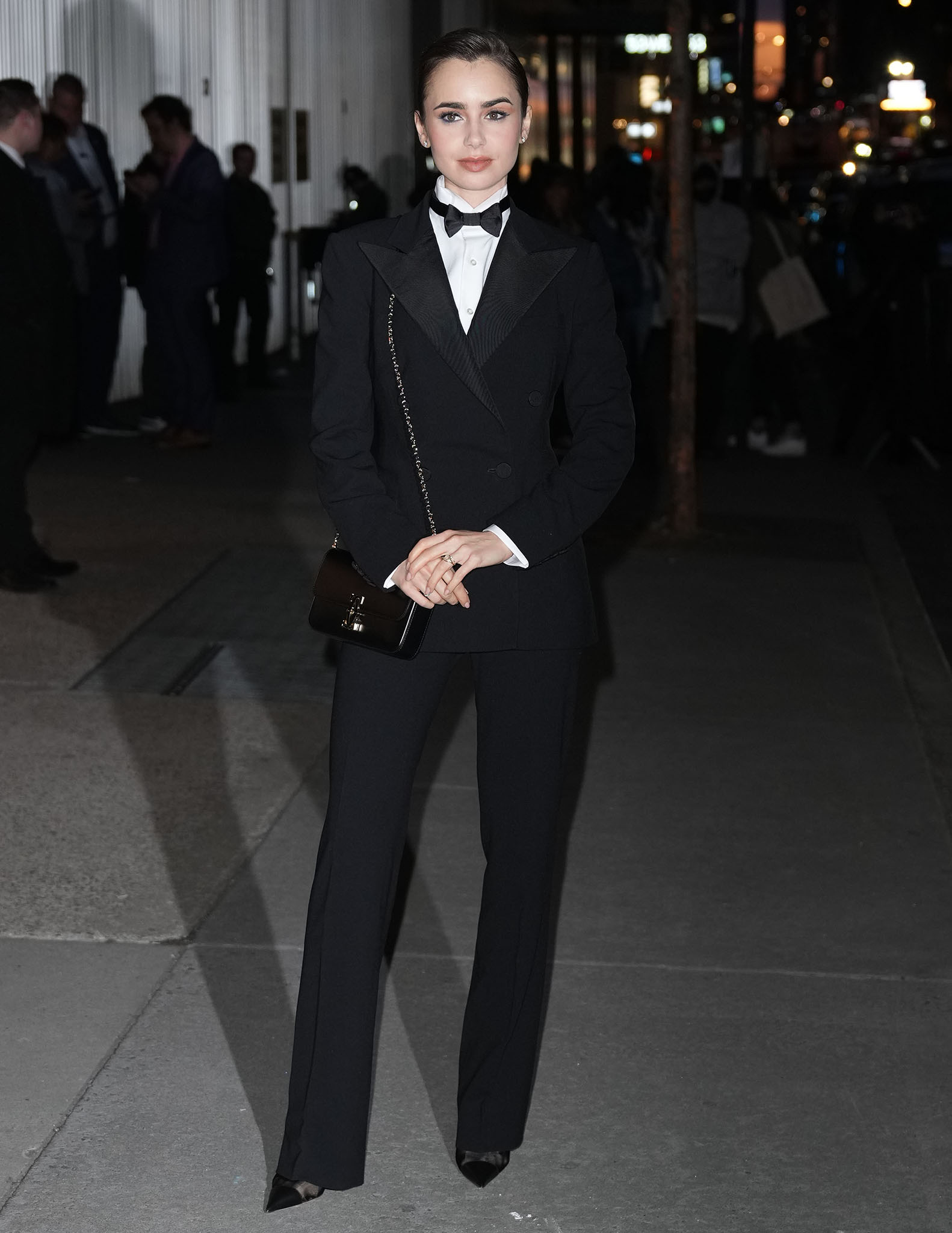 Lily Collins traded her signature feminine Emily in Paris style for a sharply tailored Ralph Lauren tuxedo, finishing the menswear-inspired look with pointed-toe black leather-and-mesh pumps and a Cartier Double C mini bag