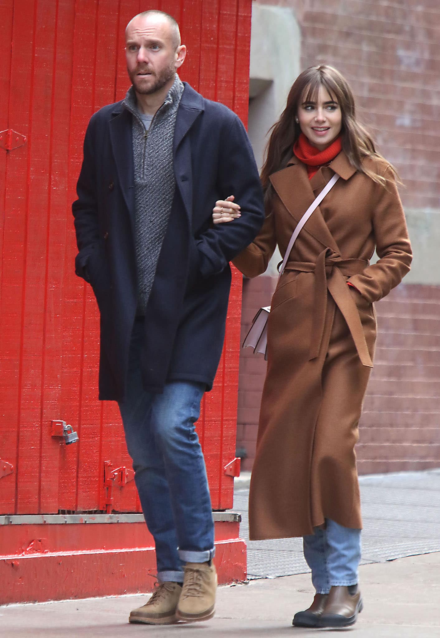 Lily Collins layered a brown belted wool coat over a bright red turtleneck and cuffed jeans for a stroll through Soho, completing the casual look with classic brown leather Chelsea boots and a blush crossbody bag