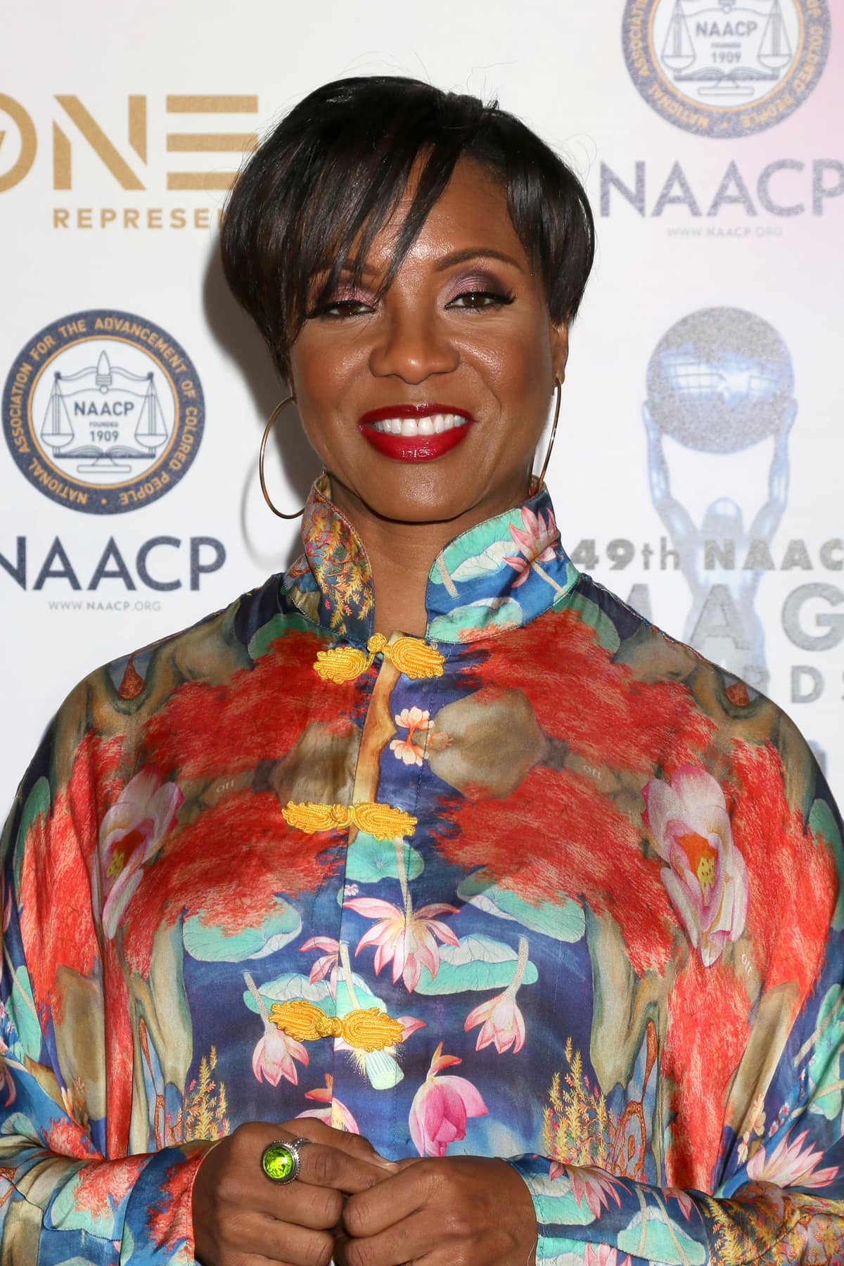 MC Lyte radiates elegance in a vibrant, floral-patterned mandarin-collar dress featuring golden frog closures and bold red lipstick at the NAACP Image Awards
