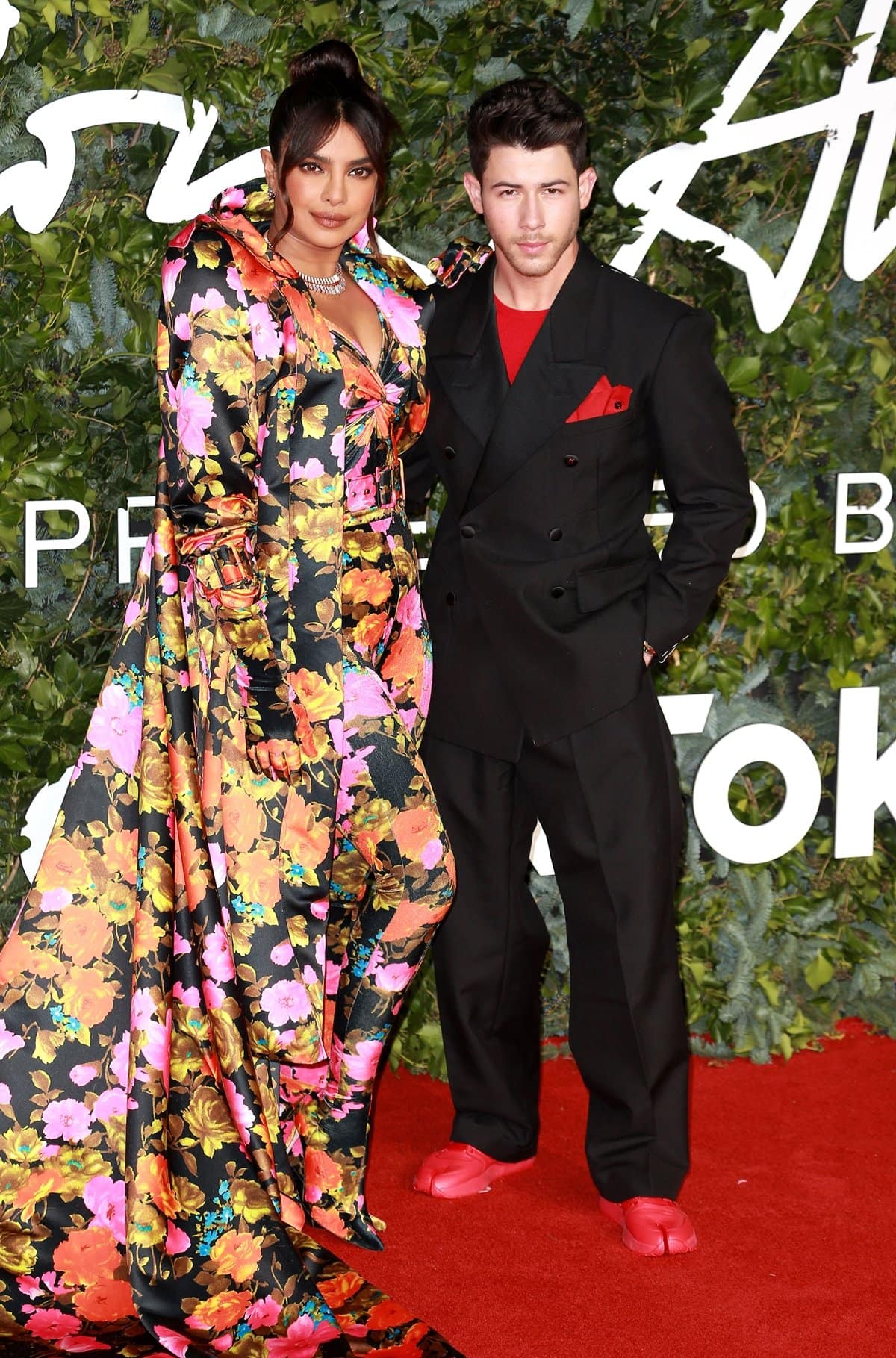 Priyanka Chopra in a Richard Quinn Fall 2021 dress and her husband Nick Jonas in a Maison Margiela Icons black tuxedo paired with red Maison Margiela x Reebok red classic leather Tabi sneakers