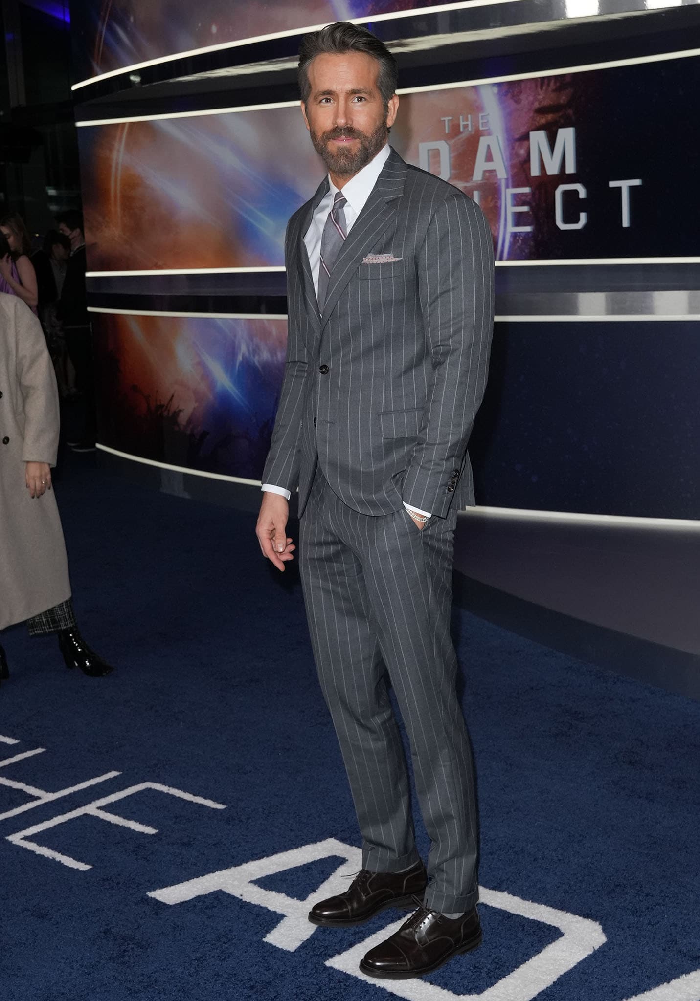 Ryan Reynolds looks dashing in a charcoal pinstriped suit and coordinating tie, finishing the sharp premiere look with polished dark leather lace-up dress shoes that grounded the tailoring with classic sophistication