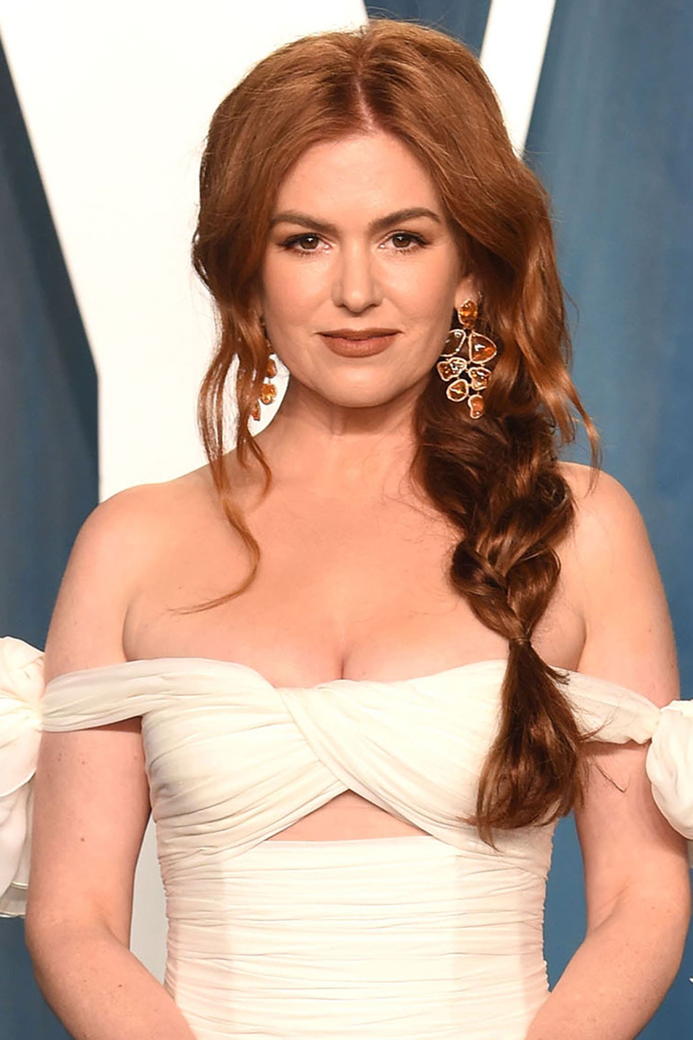 A loose side braid, warm-toned statement earrings, and restrained makeup complete Fisher's refined take on modern red-carpet dressing
