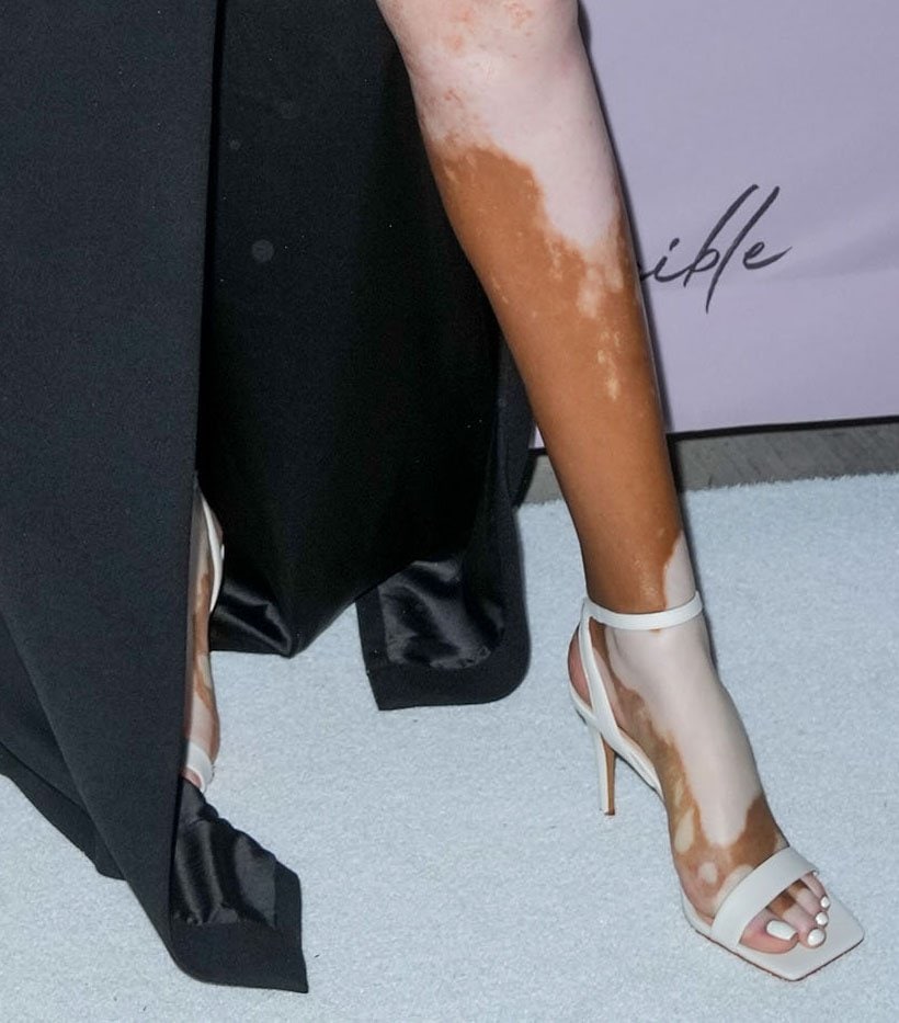 Minimalist white ankle-strap sandals provide a striking contrast against the flowing black skirt, emphasizing every step.