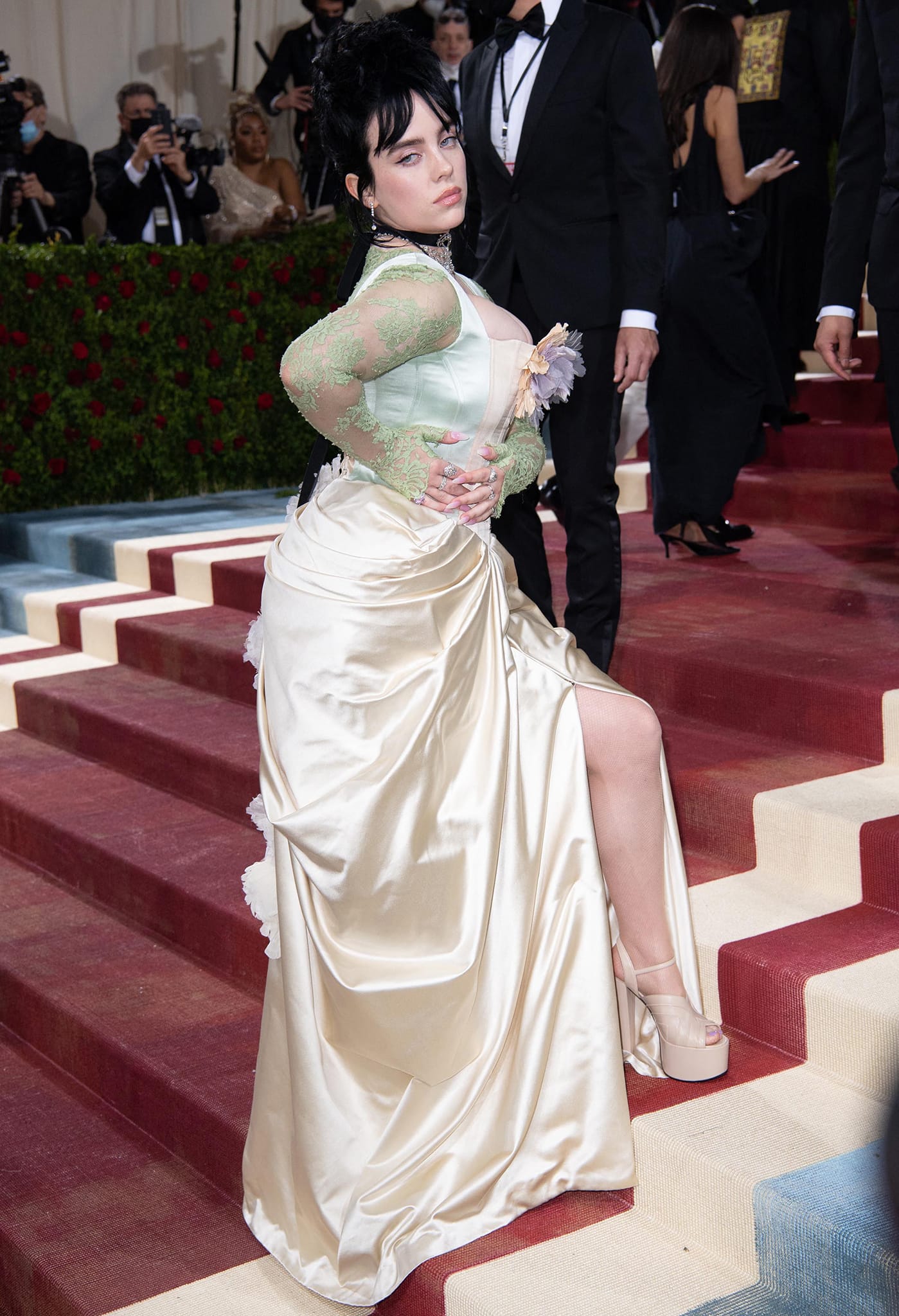 At the 2022 Met Gala in New York City, Billie Eilish styled a custom Gucci ivory duchesse satin gown with a sculpted bustle and sheer mint-green lace sleeves, pairing the romantic, vintage-inspired silhouette with towering beige platform sandals that subtly lifted the hem and added modern edge to the gilded look