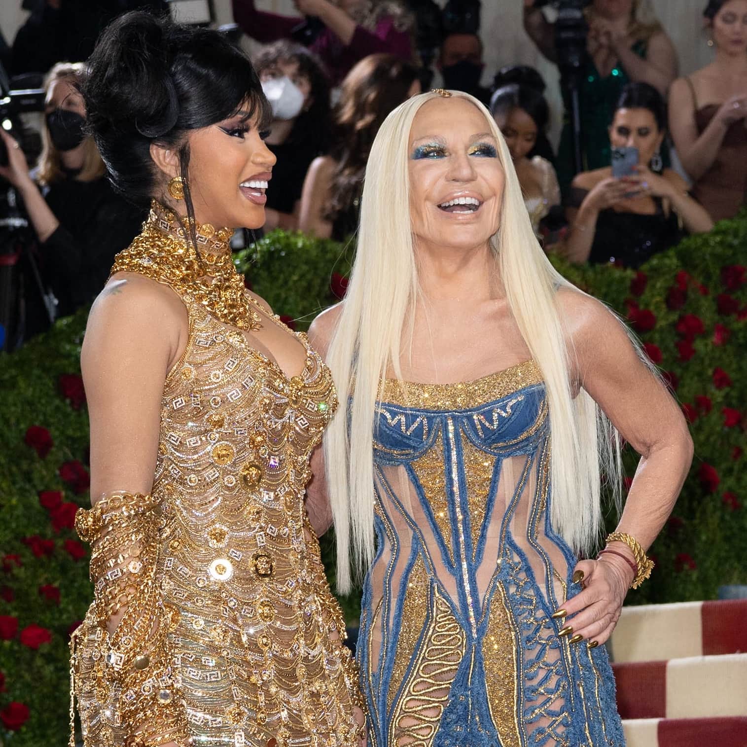 Cardi B’s intricate Versace look brings Greca borders, Medusa medallions, crystals, and layers of gold chains into focus beside Donatella Versace’s denim-and-gold detailing