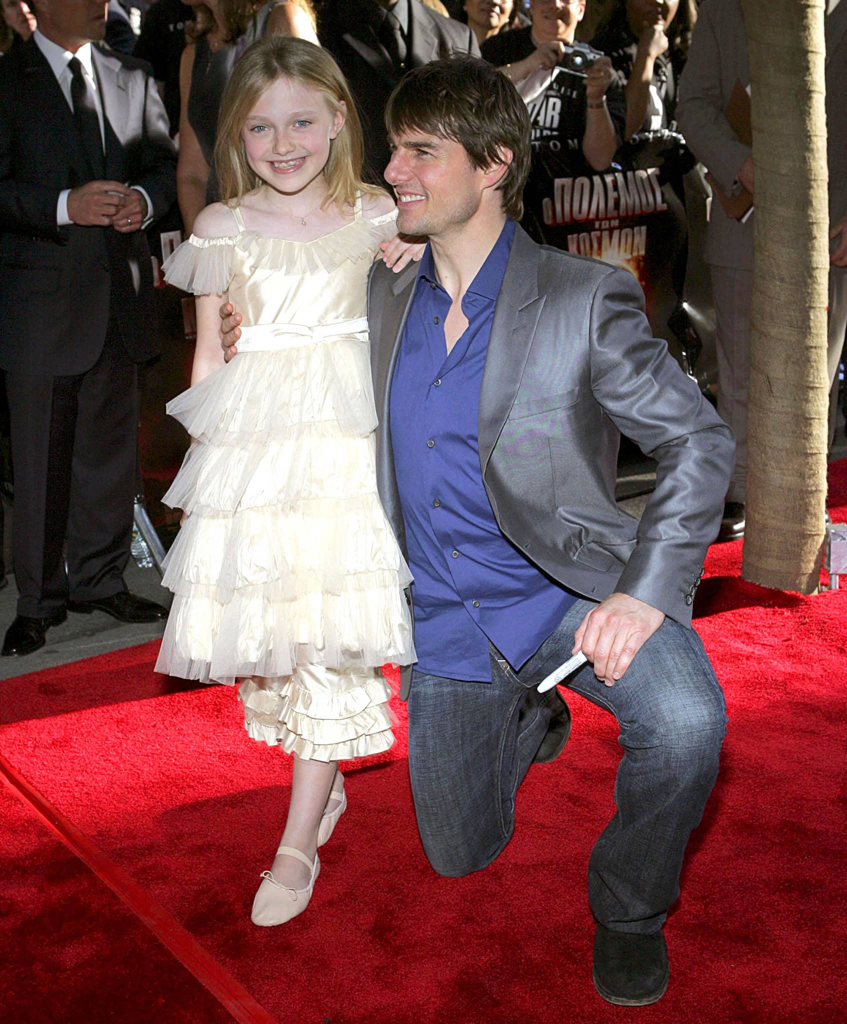 Dakota Fanning arrives with Tom Cruise at the War of the Worlds U.S. premiere on June 23, 2005, wearing a tiered ivory chiffon dress paired with delicate ballet flats—an age-appropriate red-carpet look that highlighted her polished child-star style
