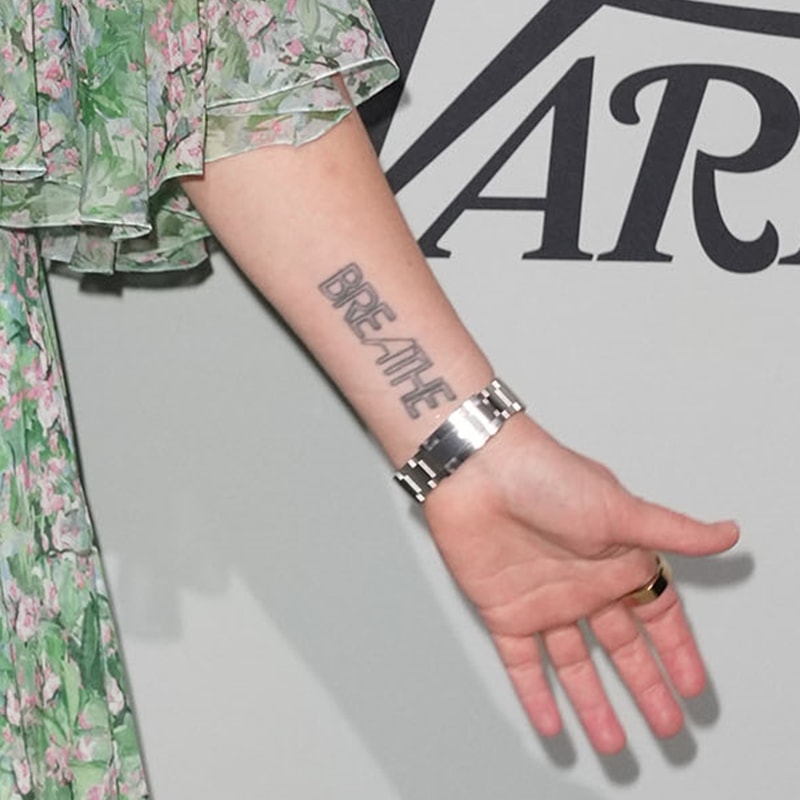 Her “BREATHE” tattoo peeks through the gown’s flutter sleeve—a subtle reminder of mindfulness that adds a personal touch to her ensemble