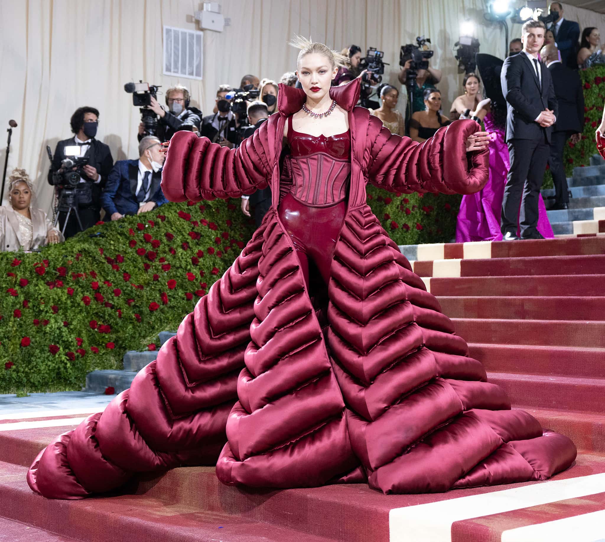 Gigi Hadid stuns in a dramatic burgundy latex and silk Versace ensemble, featuring a sculpted corset and voluminous puffer cape, at the 2022 Met Gala